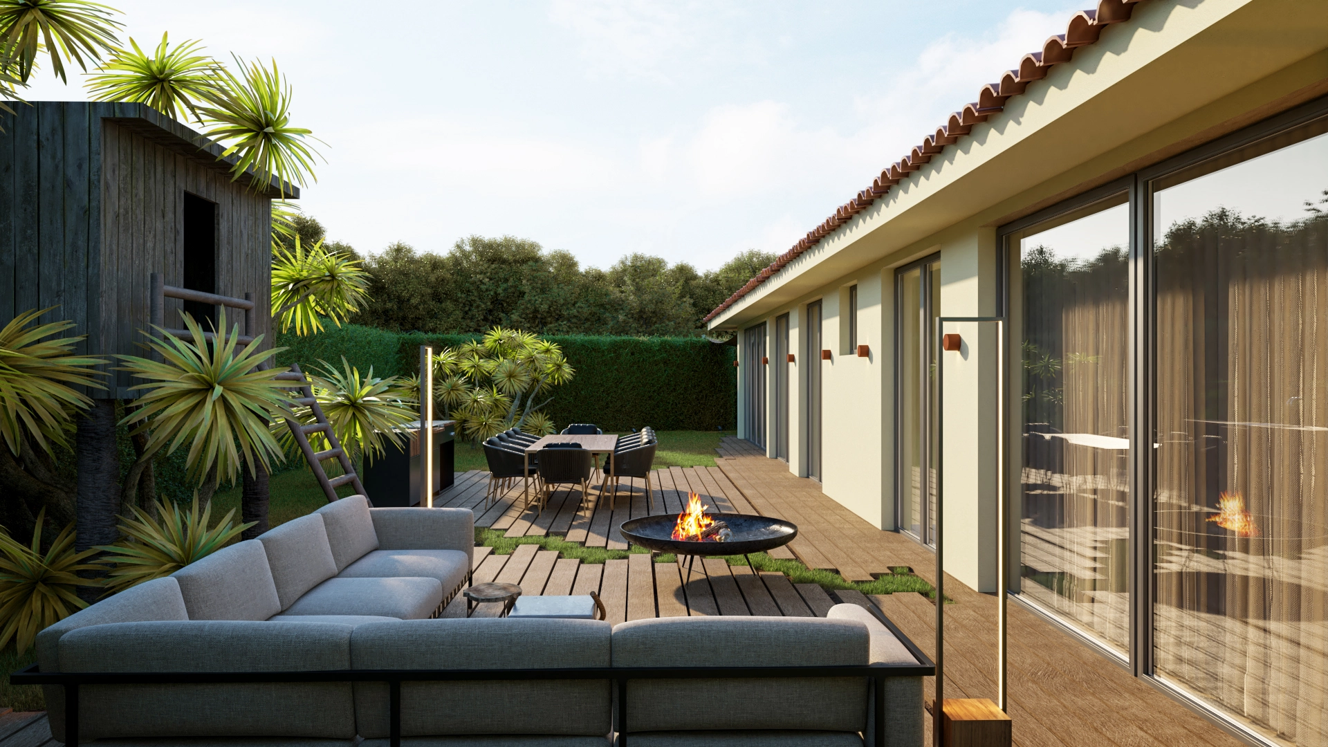 Zona de estar exterior com sofás cinzentos e braseiro sobre deck em madeira, com mesa de refeições ao fundo e vegetação envolvente.