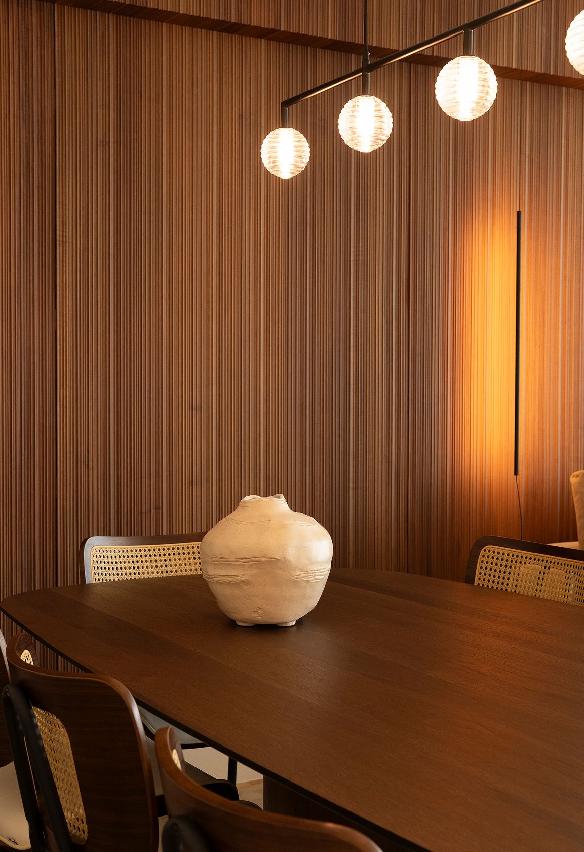 Linear suspension with ribbed glass globes, cane-back dining chairs and slatted wood wall — luxury décor details