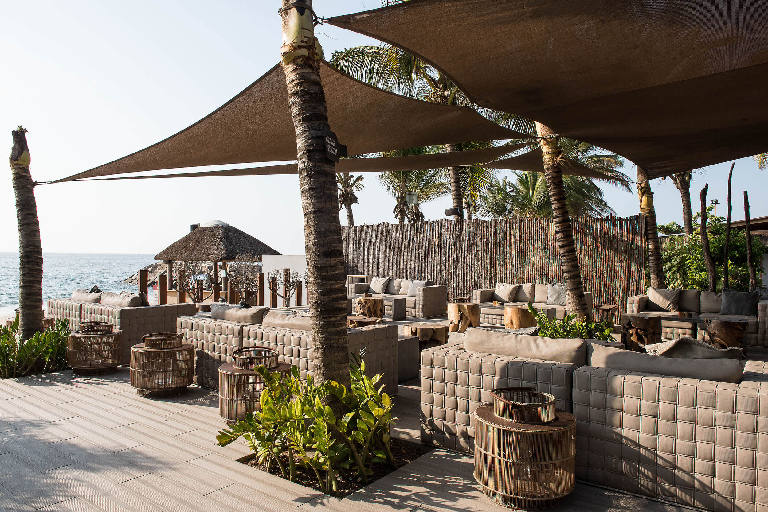 Lounge frente mar com palhota de colmo, toldos e mesas de rattan — design de interiores de restaurante de luxo Luanda, Angola