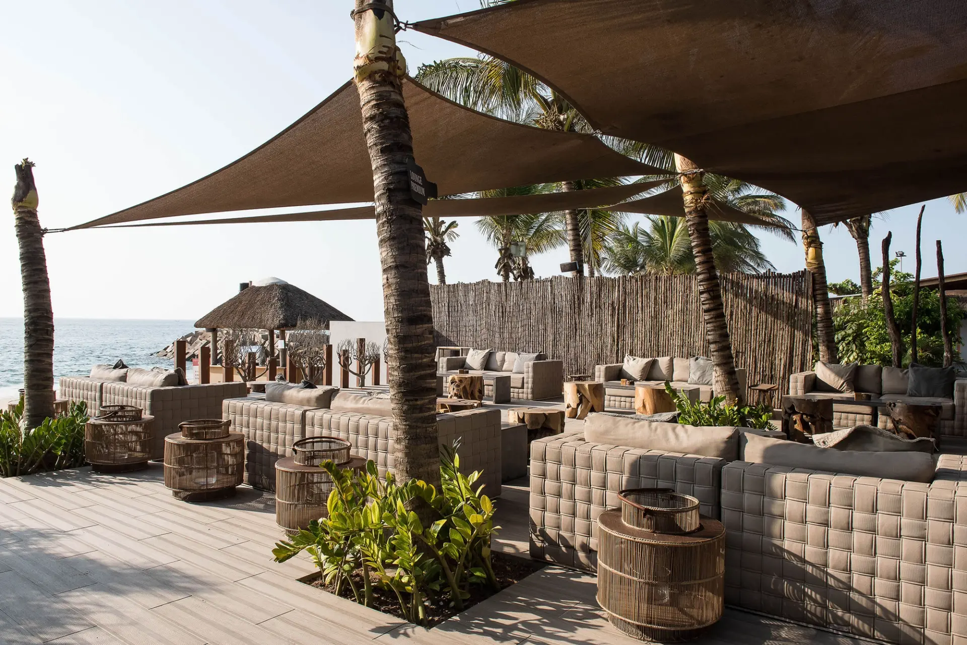 Lounge frente mar com palhota de colmo, toldos e mesas de rattan — design de interiores de restaurante de luxo Luanda, Angola