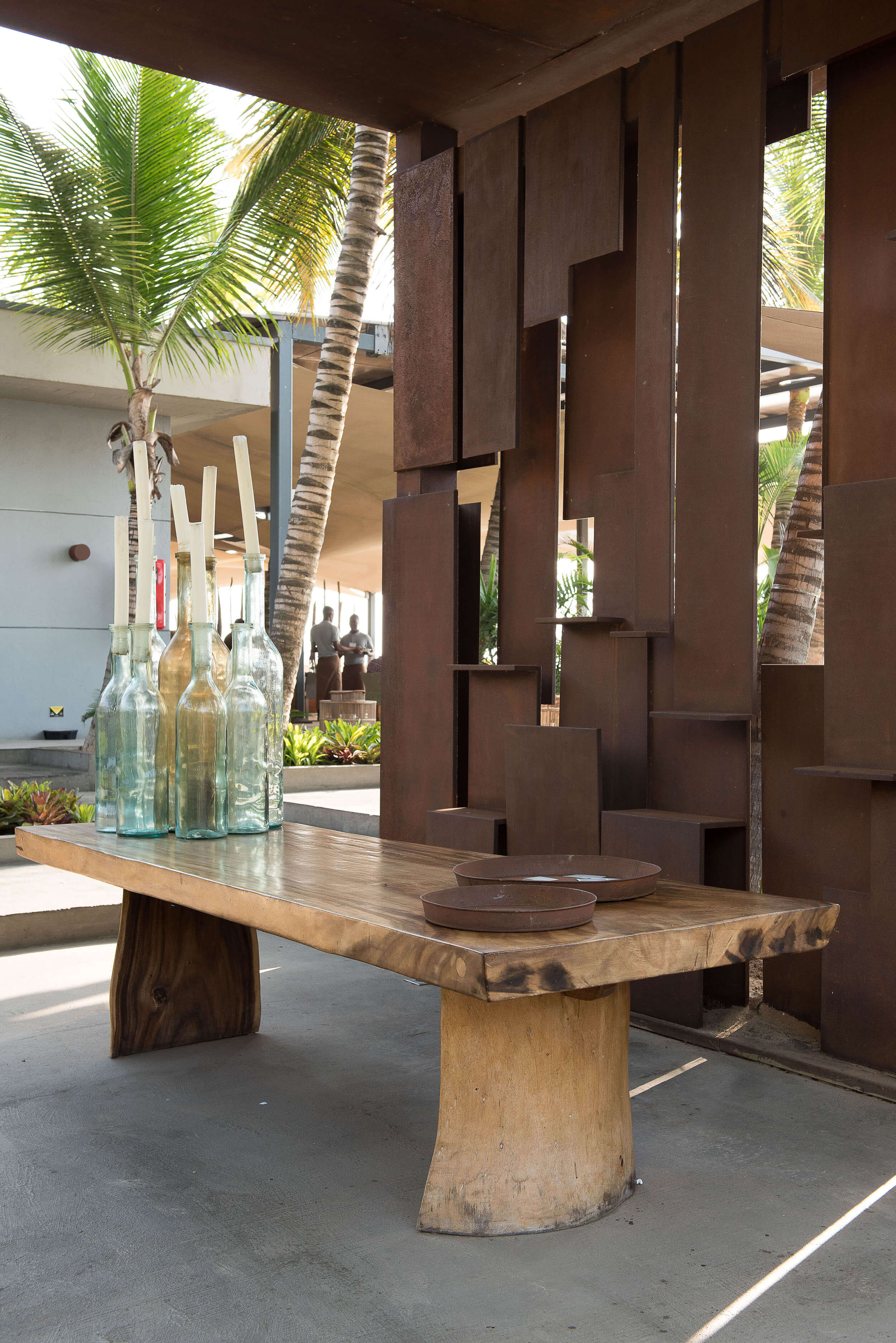 Esplanada com mesa de madeira maciça, garrafas de vidro e biombo metálico — design de interiores de restaurante de luxo Luanda, Angola