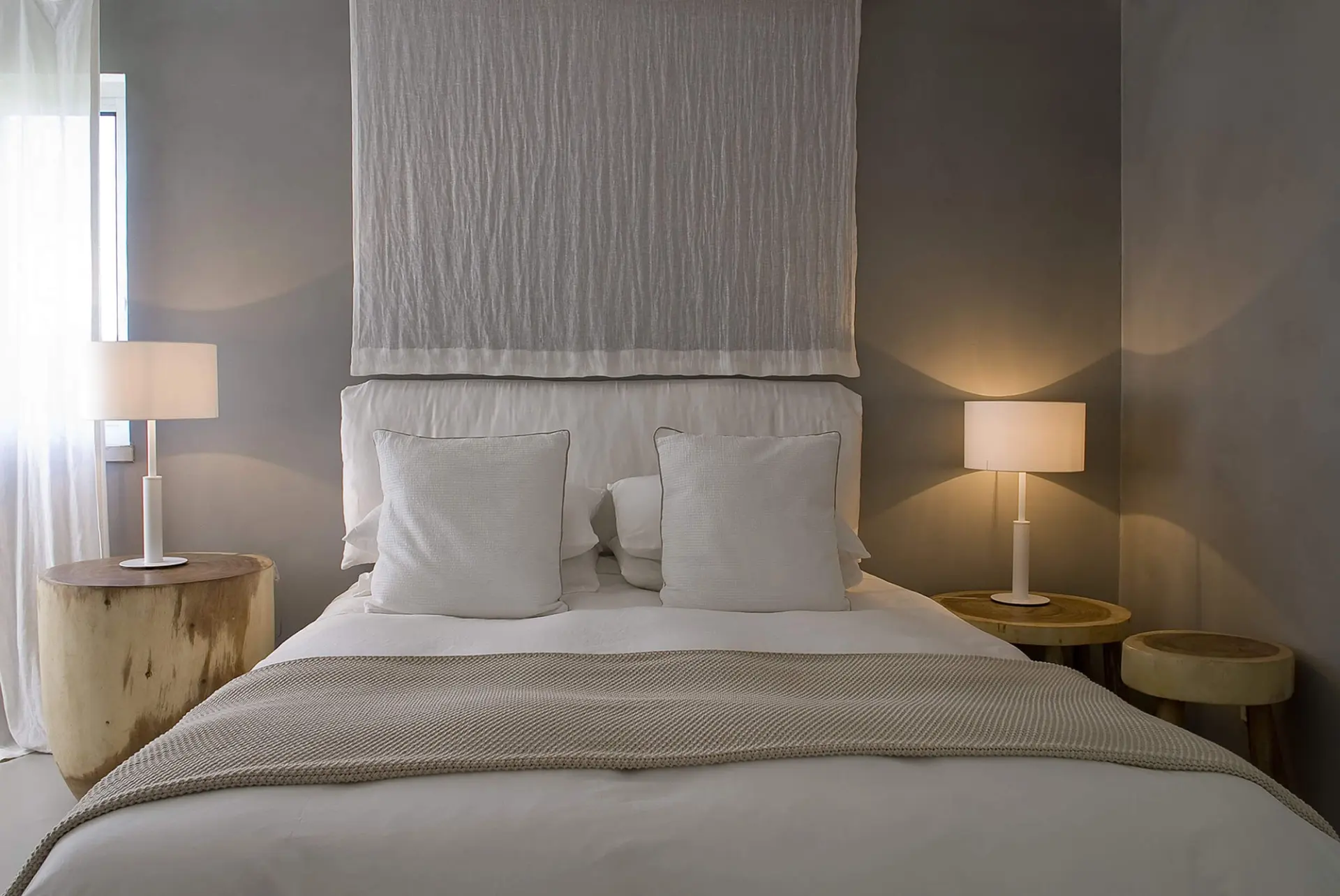 Quarto com painel têxtil drapeado, parede em microcimento e mesas em tronco — design de interiores de luxo Tróia, Setúbal