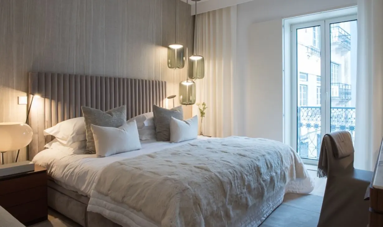 Quarto contemporâneo em apartamento de Sintra, com cabeceira estofada, paleta neutra, iluminação integrada e luz natural abundante.