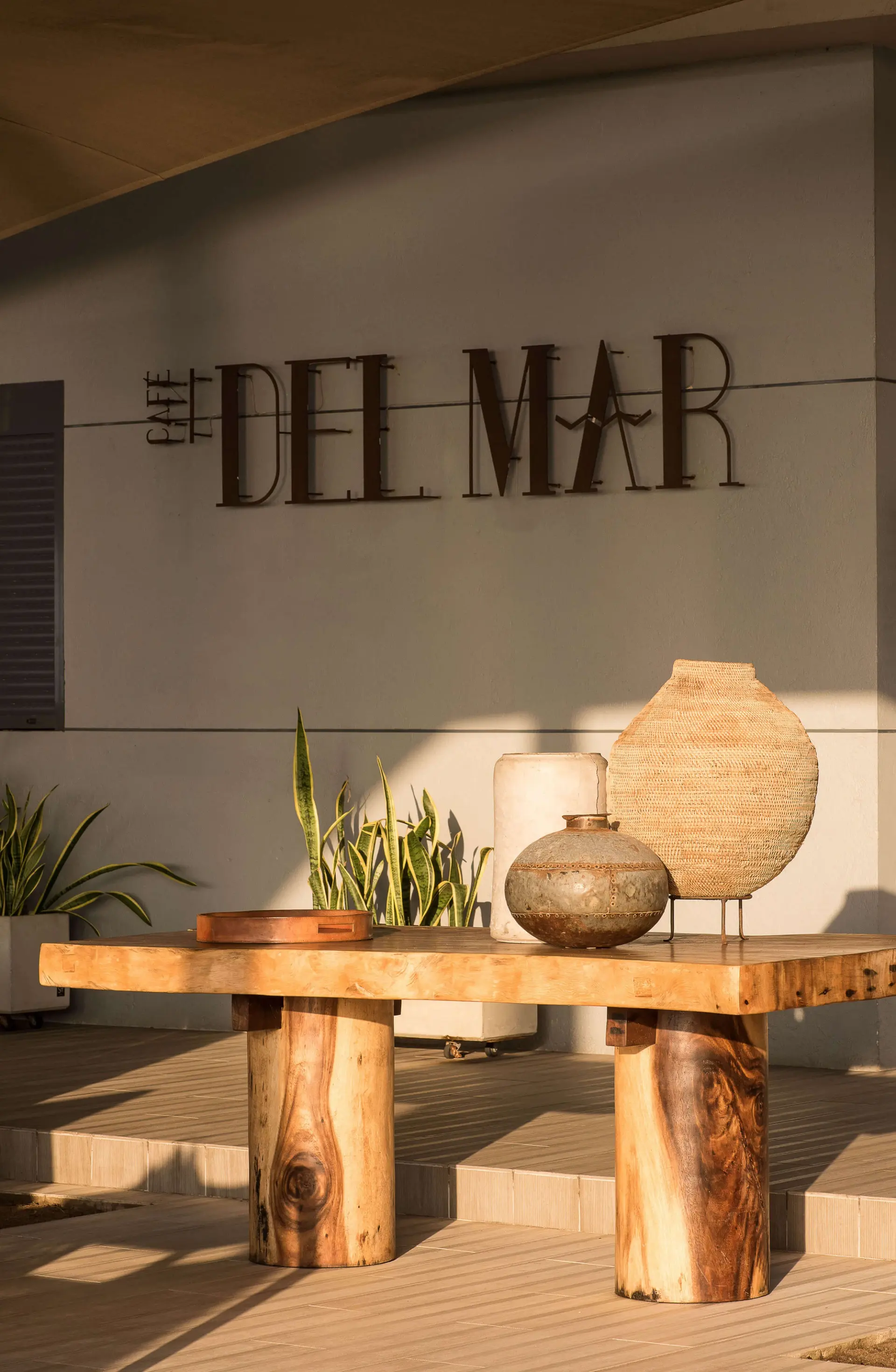 Entrada do Café Del Mar com mesa de madeira maciça e vasos cerâmicos — design de interiores de restaurante de luxo Luanda, Angola