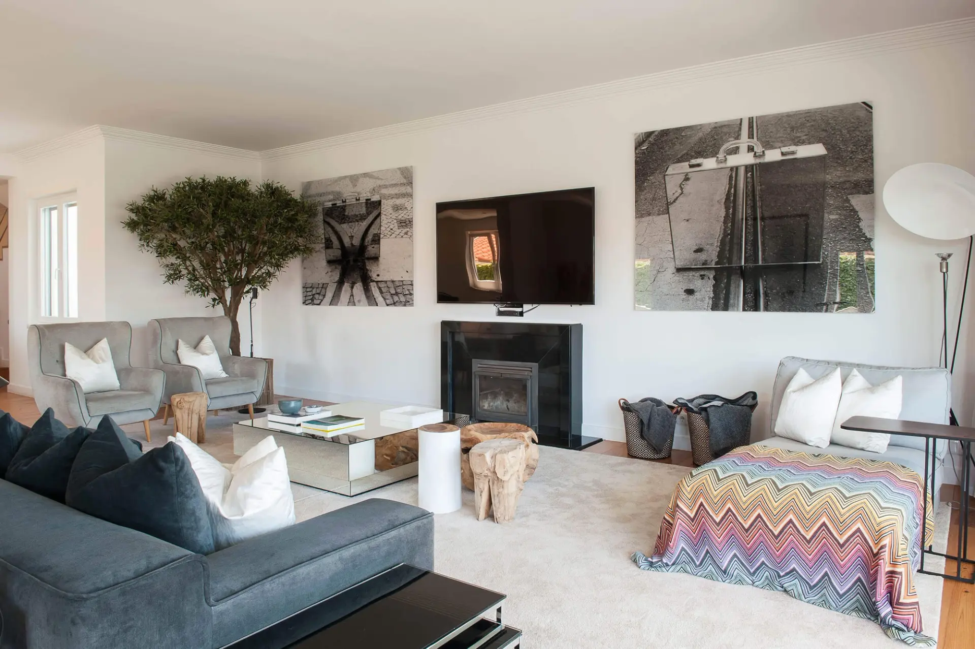 Large cobblestone photographs, grey velvet sofas, a mirrored coffee table and wood-stump stools by a fireplace — luxury living room