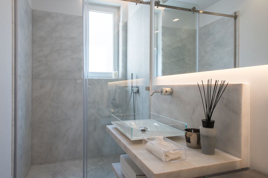 Casa de banho de master suite com revestimento em mármore, iluminação integrada, lavatório minimalista e cabine de duche em vidro.