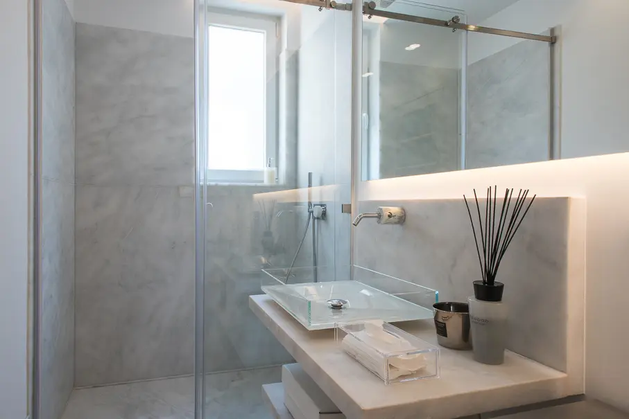 Casa de banho de master suite com revestimento em mármore, iluminação integrada, lavatório minimalista e cabine de duche em vidro.