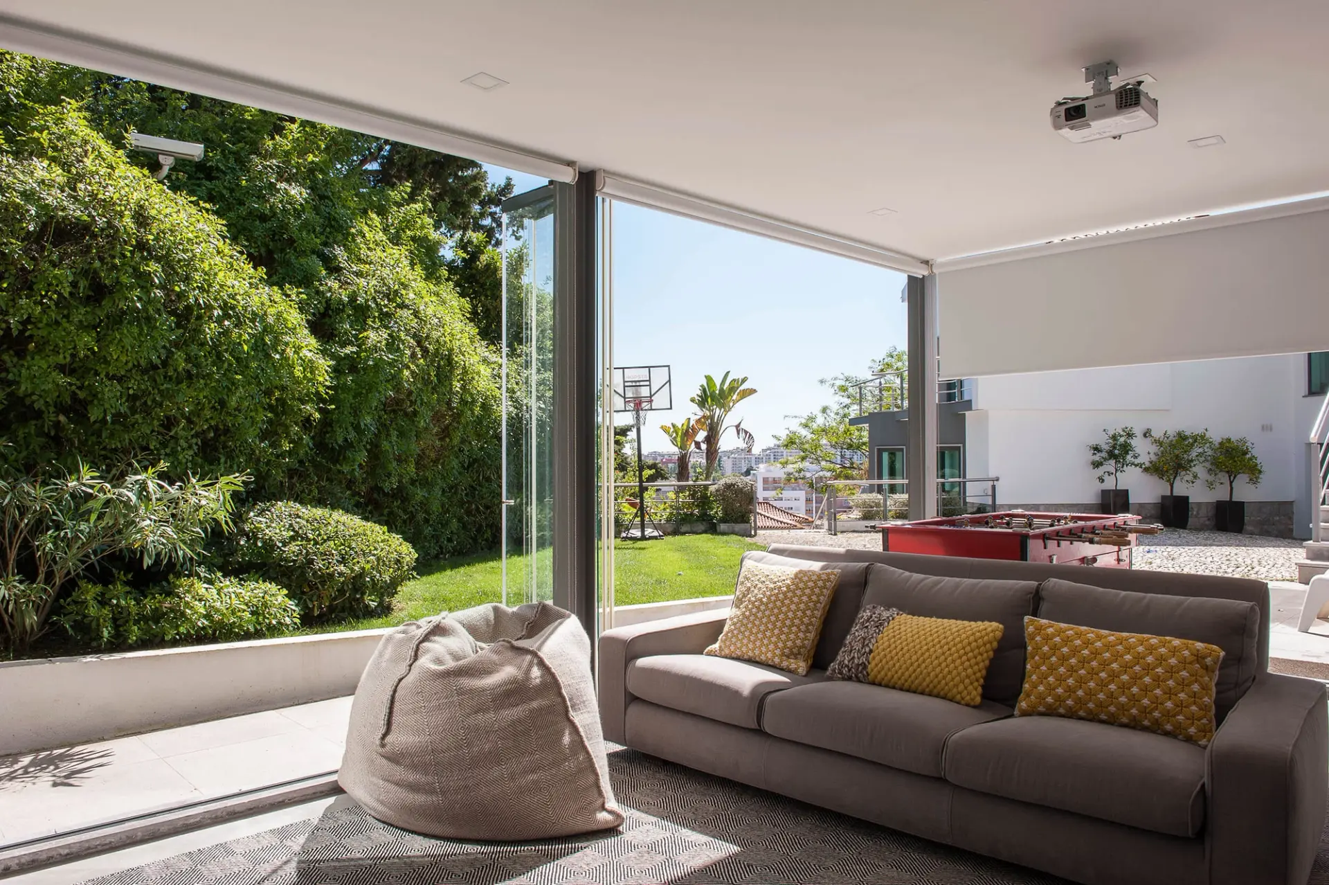 Sala jogos com sofá cinzento, almofadas Gandia Blasco amarelas, jardim e matraquilhos — design de interiores de luxo Paço de Arcos, Oeiras, Atelier Renata Santos Machado