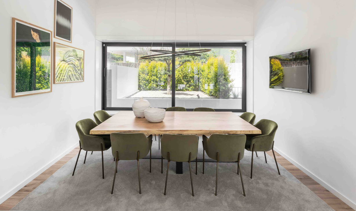 Contemporary dining room with wooden table, green chairs and large window connecting to outdoor space in an interior design project in Óbidos
