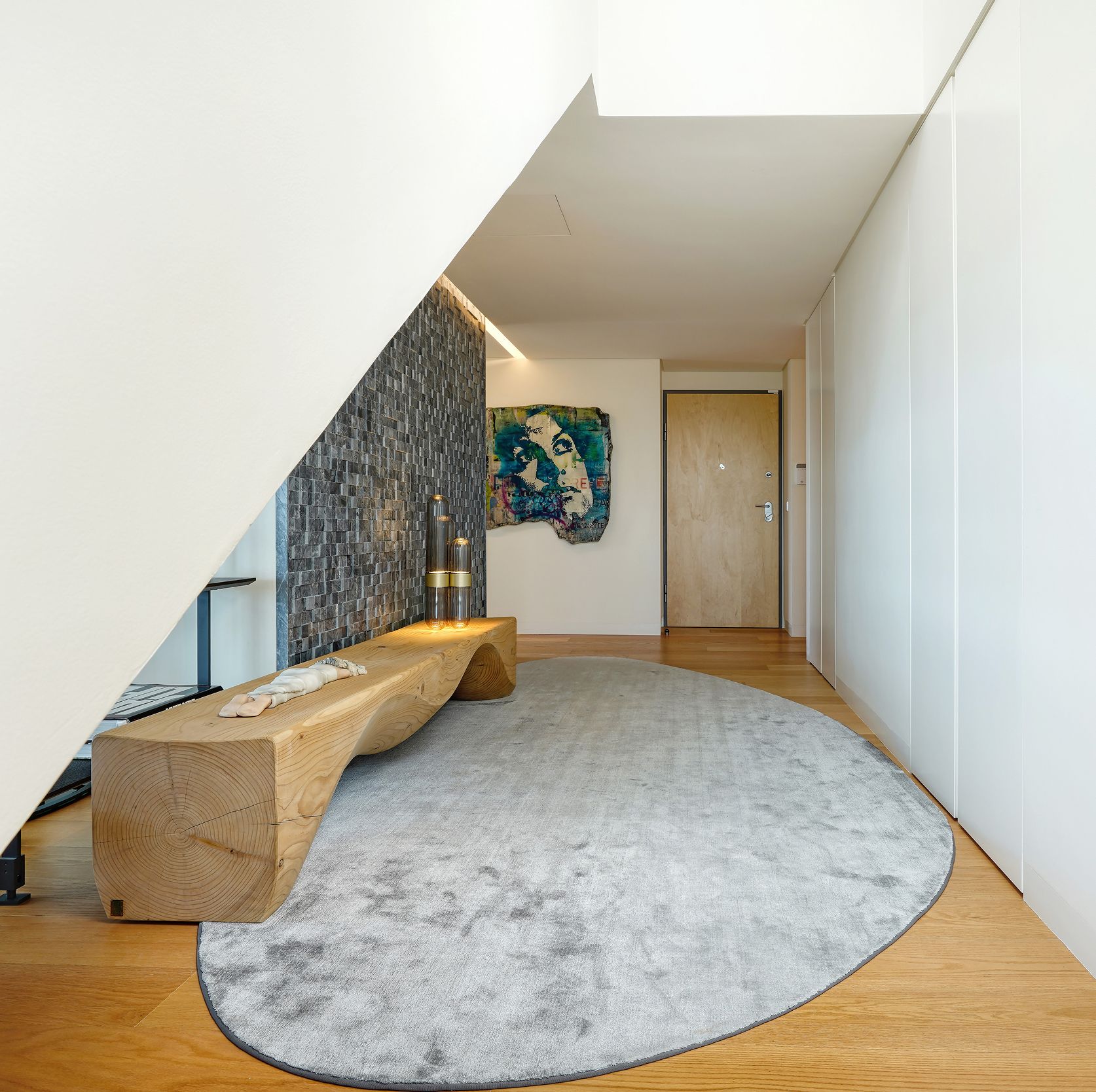 Hall de entrada de penthouse com banco em madeira natural, tapete oval cinzento e obra de arte — design de interiores de luxo na Praça de Espanha, Lisboa, Atelier Renata Santos Machado