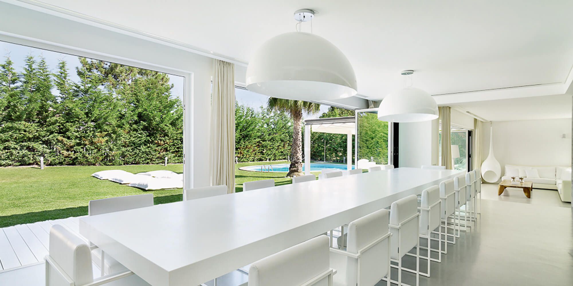 Sala de jantar minimalista com mesa em branco lacado, vista sobre jardim e piscina — projeto de design de interiores de luxo em Tróia, Portugal, Atelier Renata Santos Machado