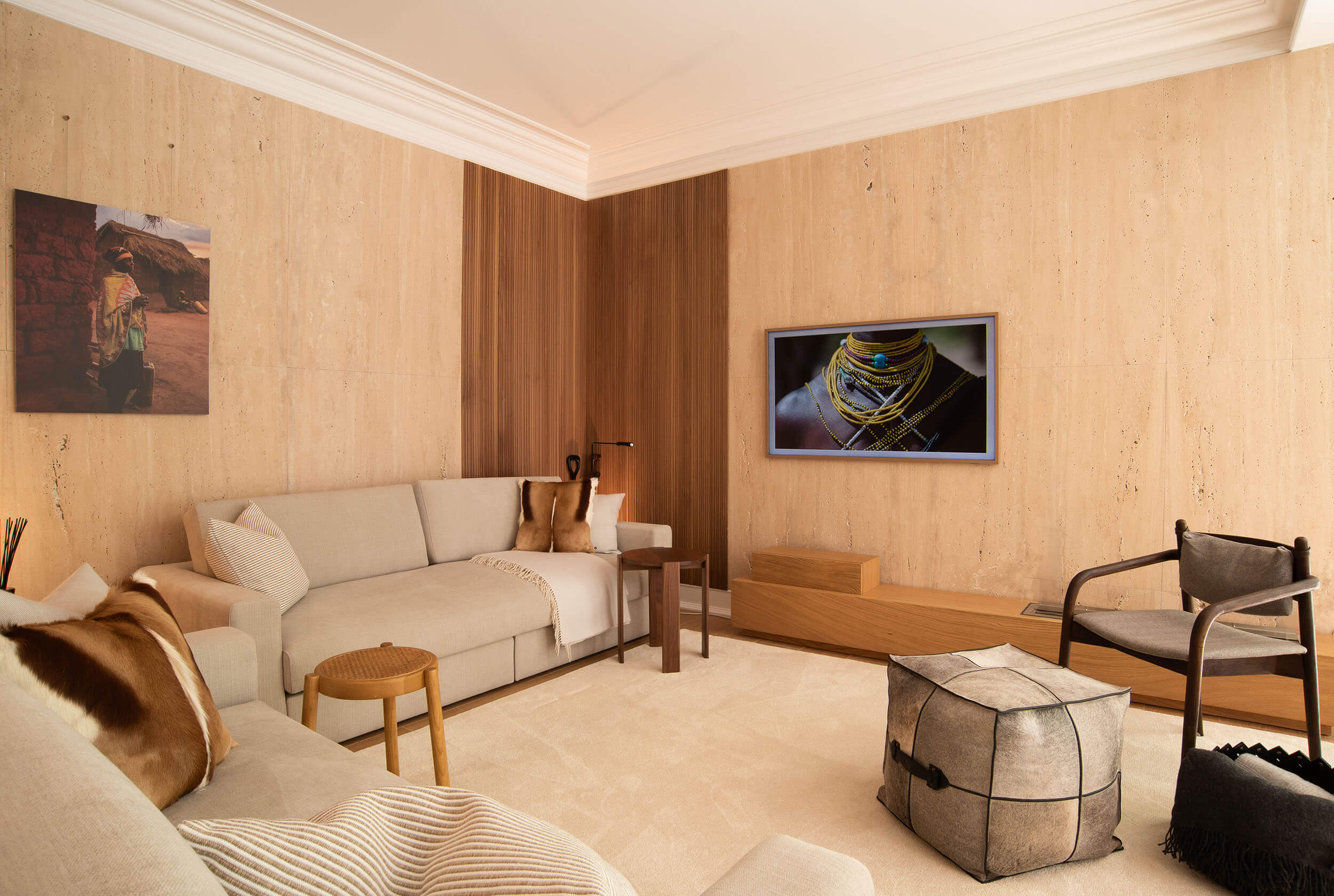 Hide cushion, walnut armchair and a woven leather bowl against travertine walls with African-themed wall art — luxury living room