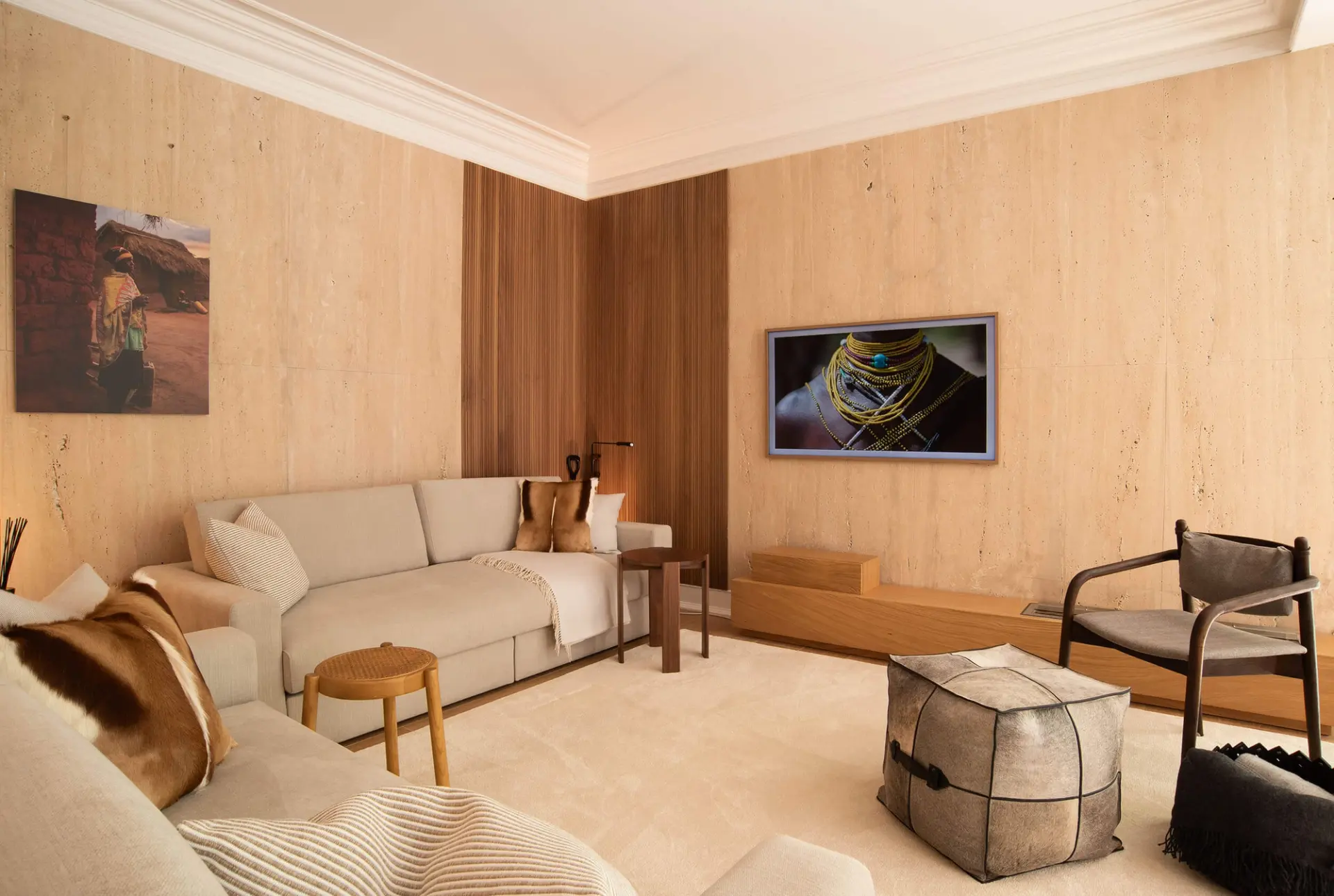 Hide cushion, walnut armchair and a woven leather bowl against travertine walls with African-themed wall art — luxury living room