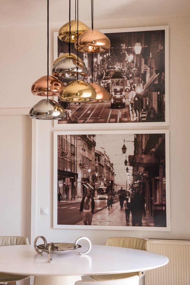 Zona de jantar com mesa branca, cadeiras claras e candeeiros suspensos em tons metálicos, junto a duas fotografias de ruas de Lisboa.