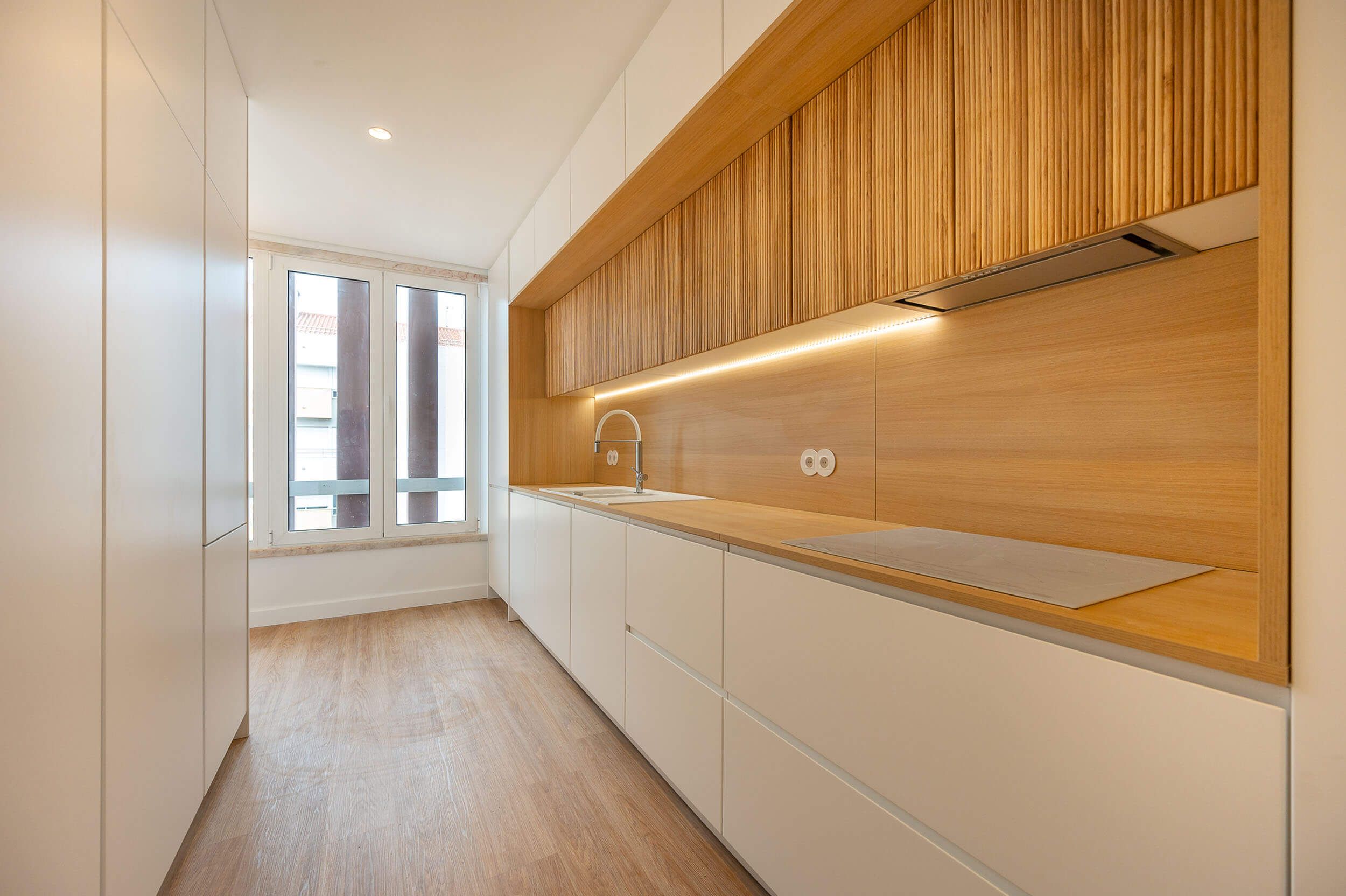 Recessed fluted oak niche over a wood worktop, white base units and an induction hob beside a window — luxury kitchen