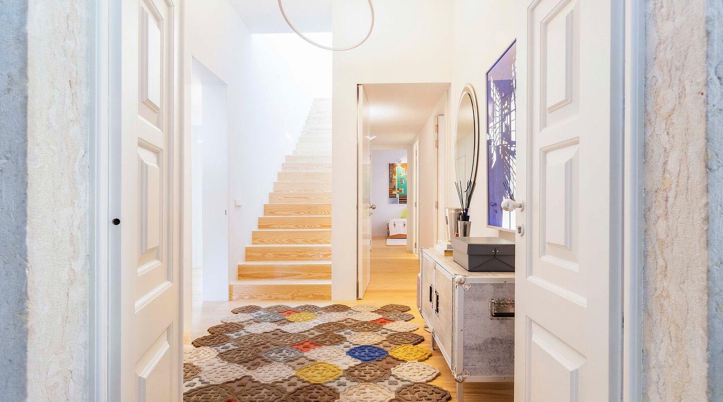 Hall de entrada luminoso com escada em madeira, tapete artesanal geométrico e espelho — design de interiores residencial em Lisboa, Atelier Renata Santos Machado