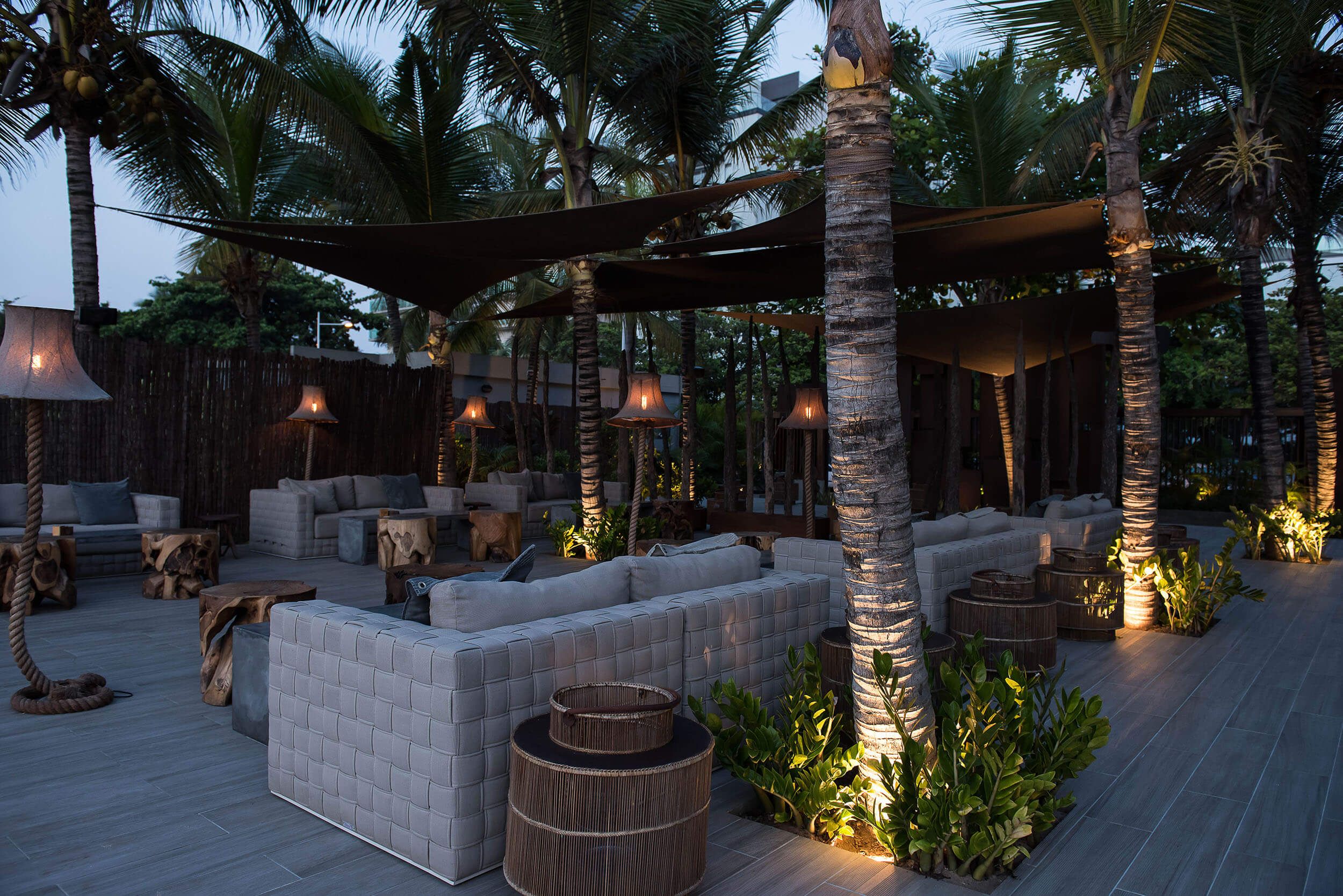 Lounge exterior ao anoitecer com candeeiros de pé e sofás trançados — design de interiores de restaurante de luxo Luanda, Angola