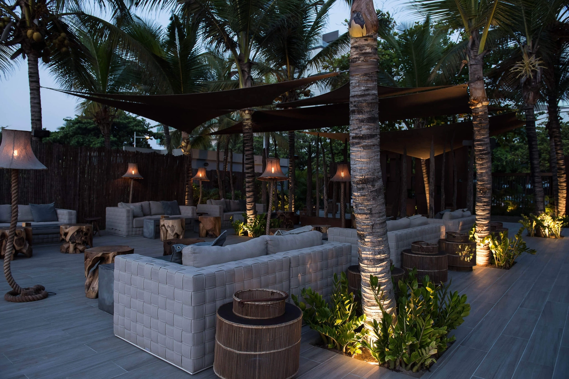 Lounge exterior ao anoitecer com candeeiros de pé e sofás trançados — design de interiores de restaurante de luxo Luanda, Angola
