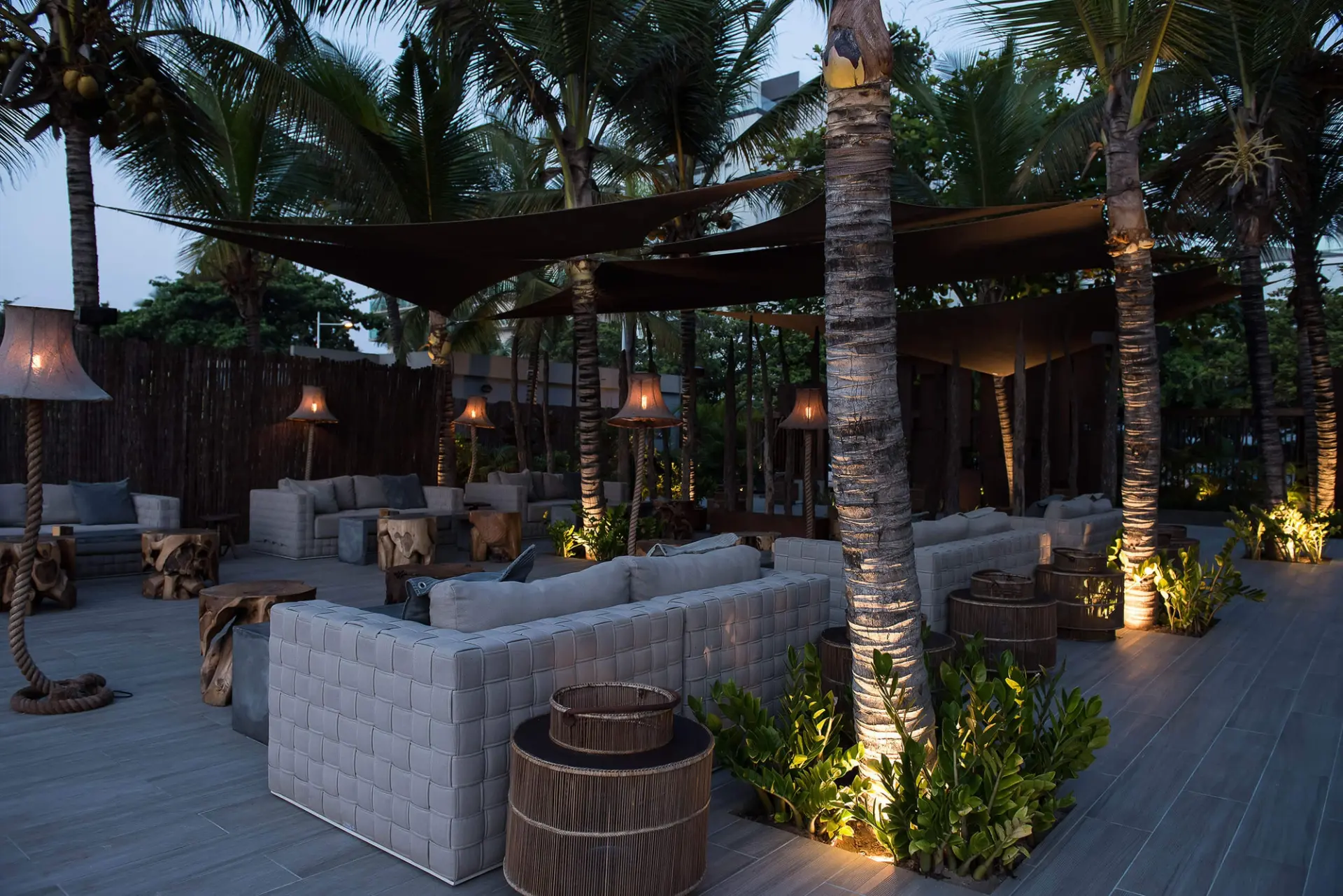 Lounge exterior ao anoitecer com candeeiros de pé e sofás trançados — design de interiores de restaurante de luxo Luanda, Angola