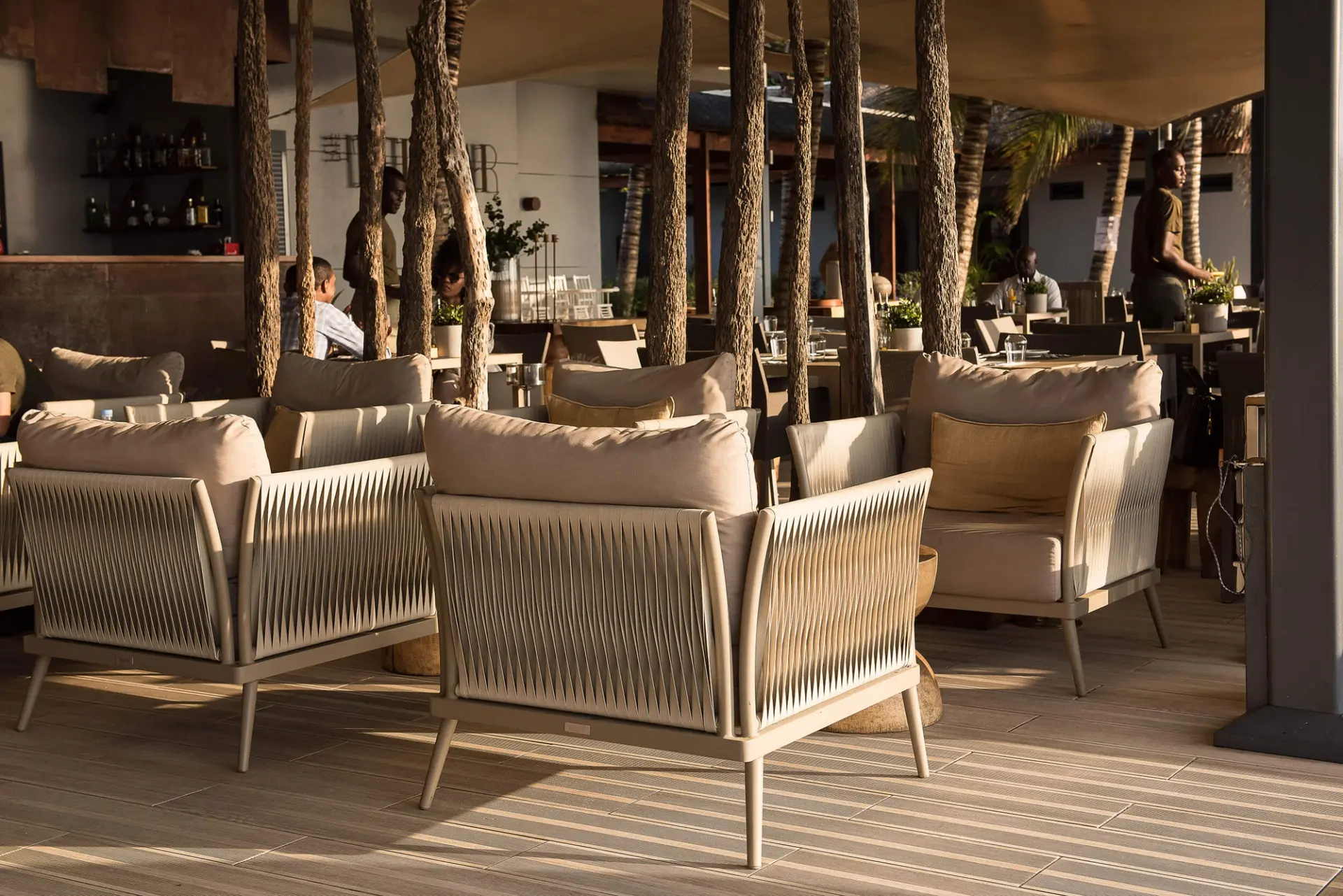 Sala interior com cadeirões em corda trançada e bar ao fundo — design de interiores de restaurante de luxo Luanda, Angola