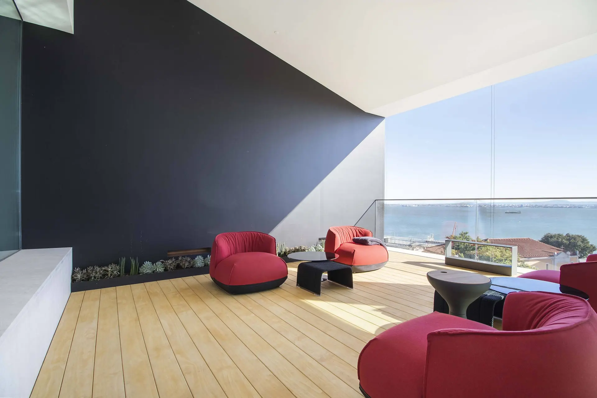 Pátio exterior com cadeirões Kristália em vermelho, poufs Paola Lenti e vista panorâmica do Tejo — design de interiores de luxo, Lisboa, Atelier Renata Santos Machado