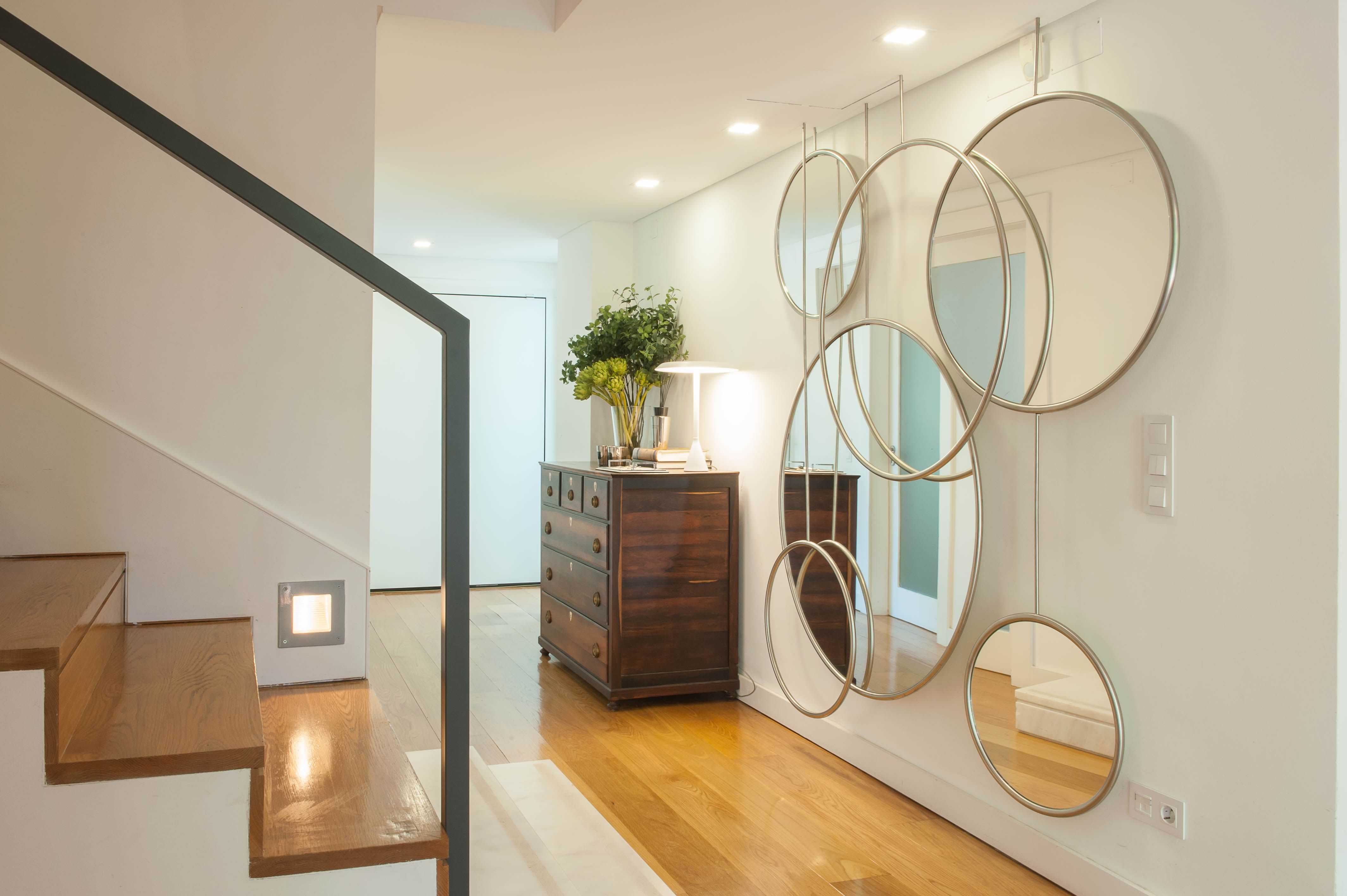 Hall contemporâneo com escada em madeira, composição de espelhos redondos e cómoda num projeto de design de interiores.