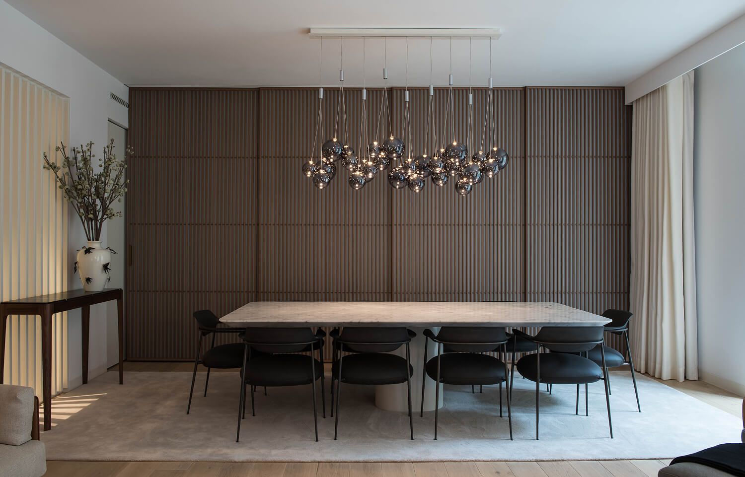 Dining room with slatted walnut sliding doors, a marble table, and a sculptural pendant light.