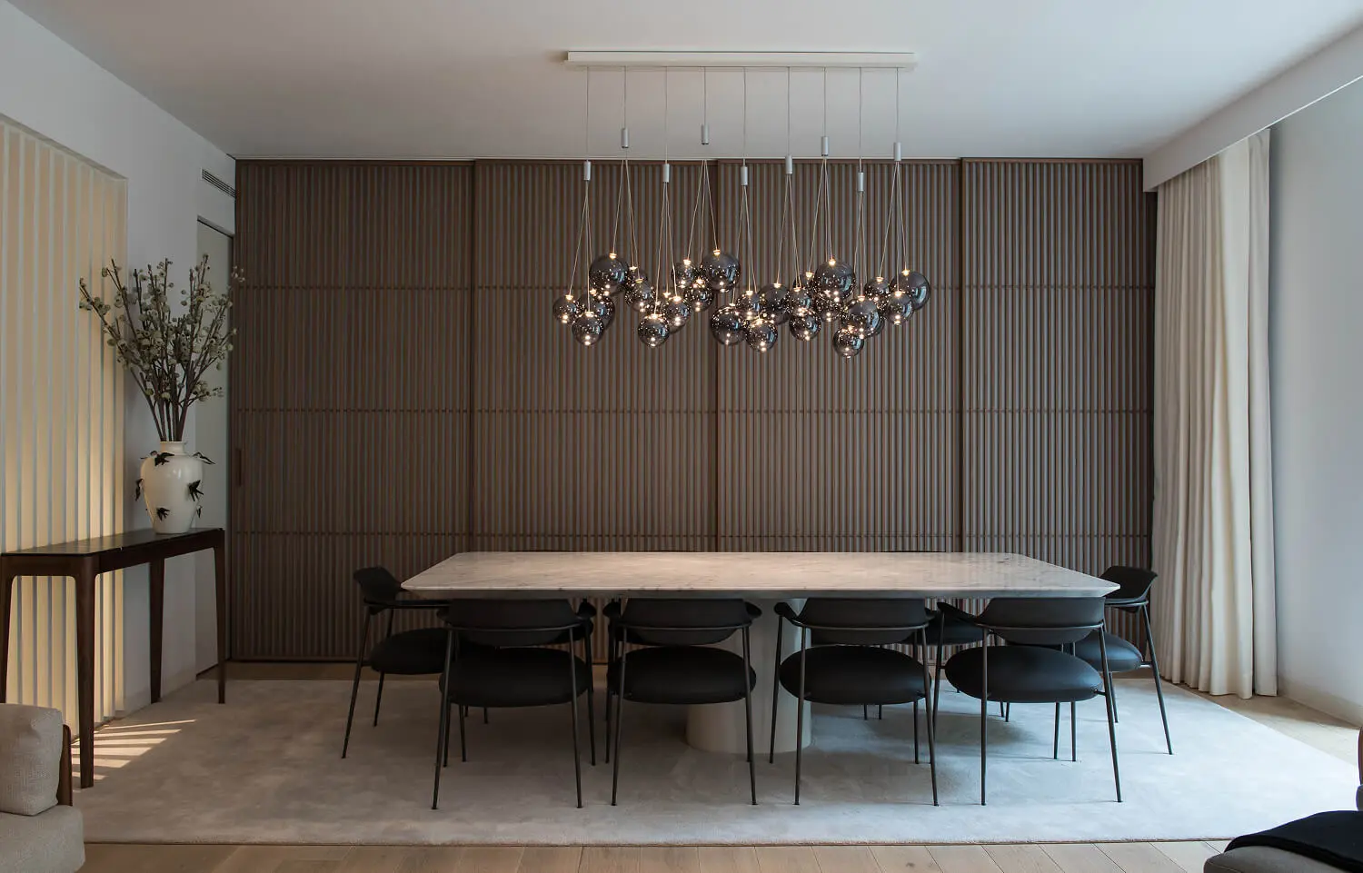 Dining room with slatted walnut sliding doors, a marble table, and a sculptural pendant light.
