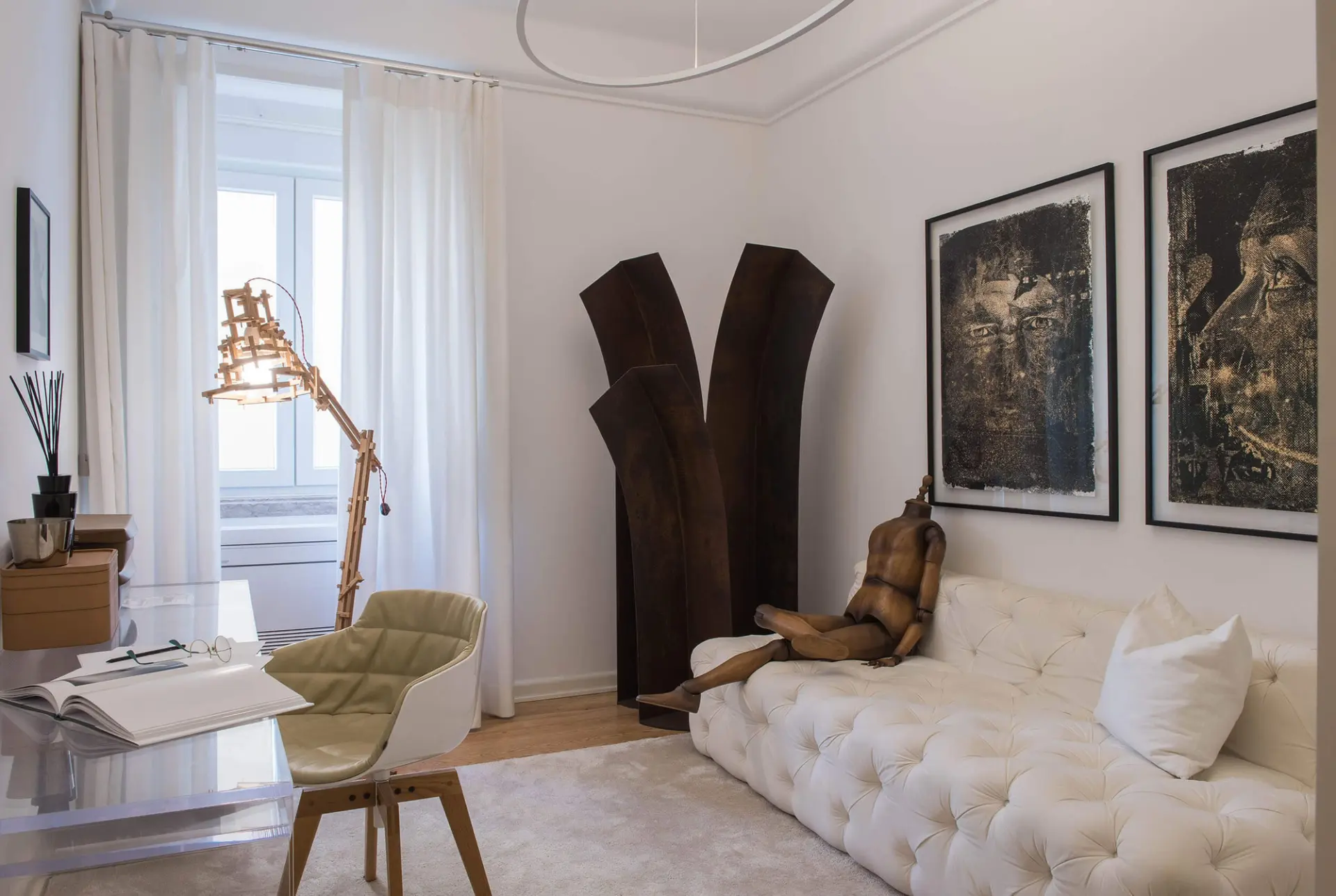 Sofá capitonné branco, candeeiro articulado em madeira e escultura em aço corten junto a retratos emoldurados — escritório de luxo