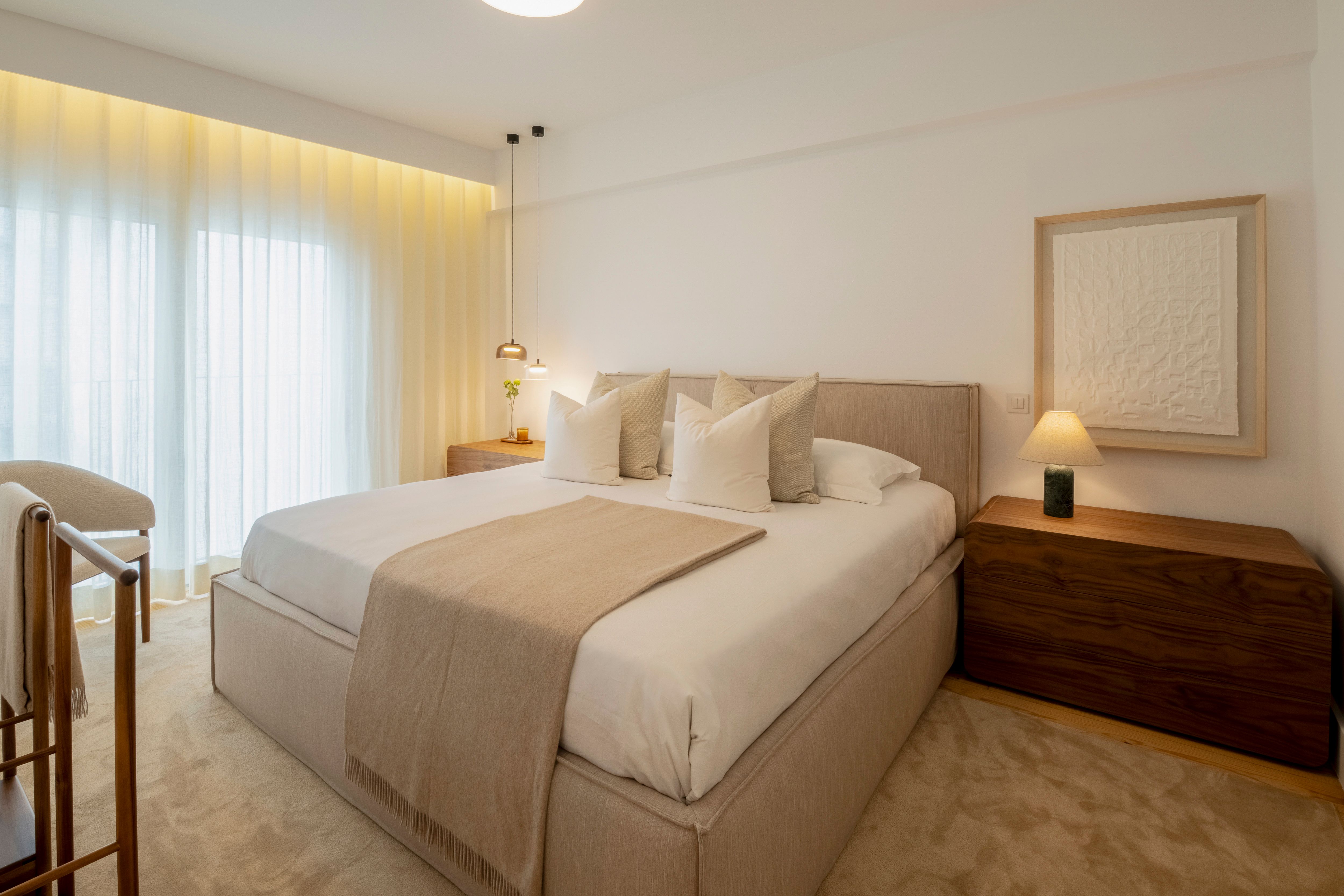 Quarto em tons neutros com cama estofada e mobiliário em madeira, num projeto do Atelier Renata Santos Machado.