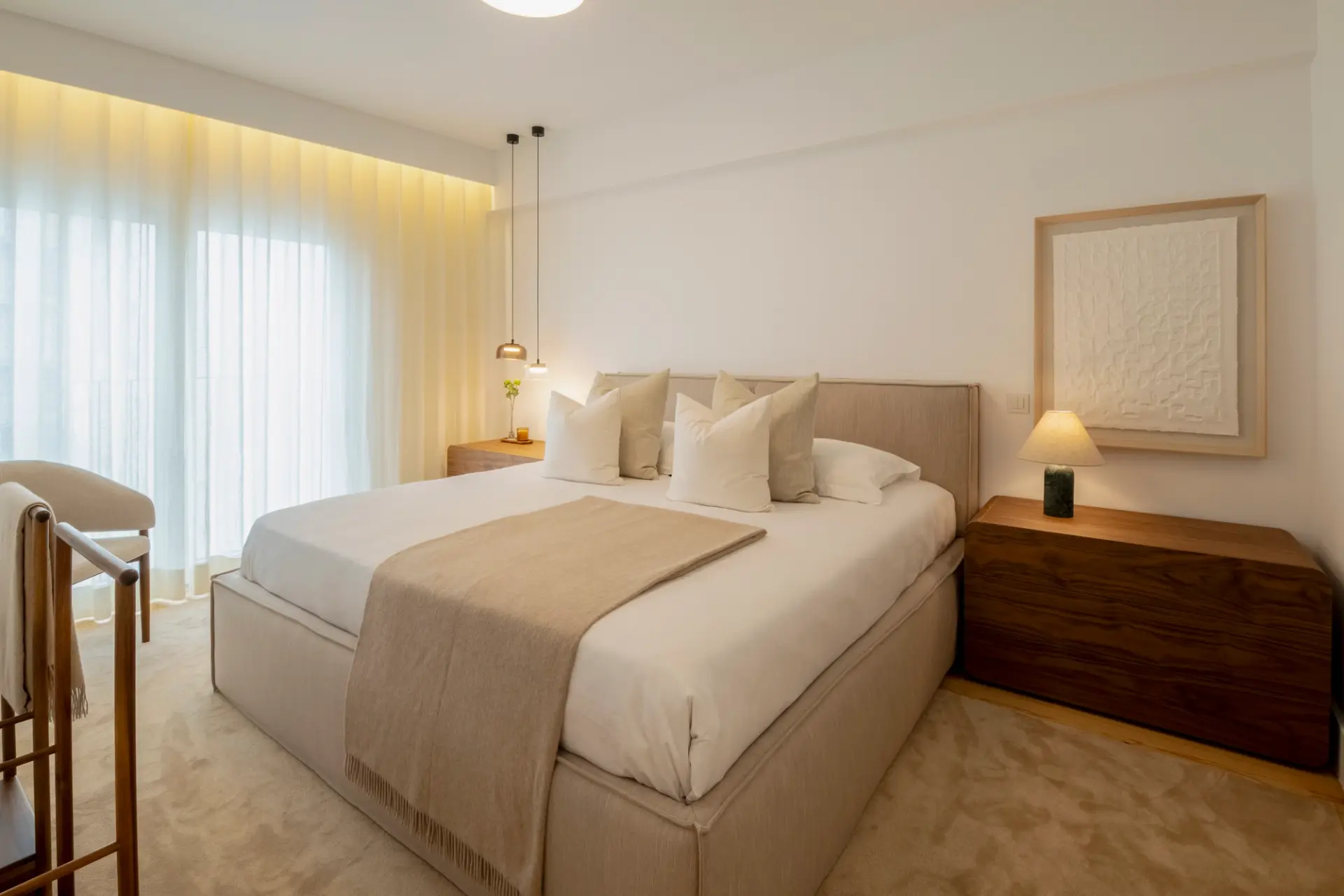 Quarto em tons neutros com cama estofada e mobiliário em madeira, num projeto do Atelier Renata Santos Machado.