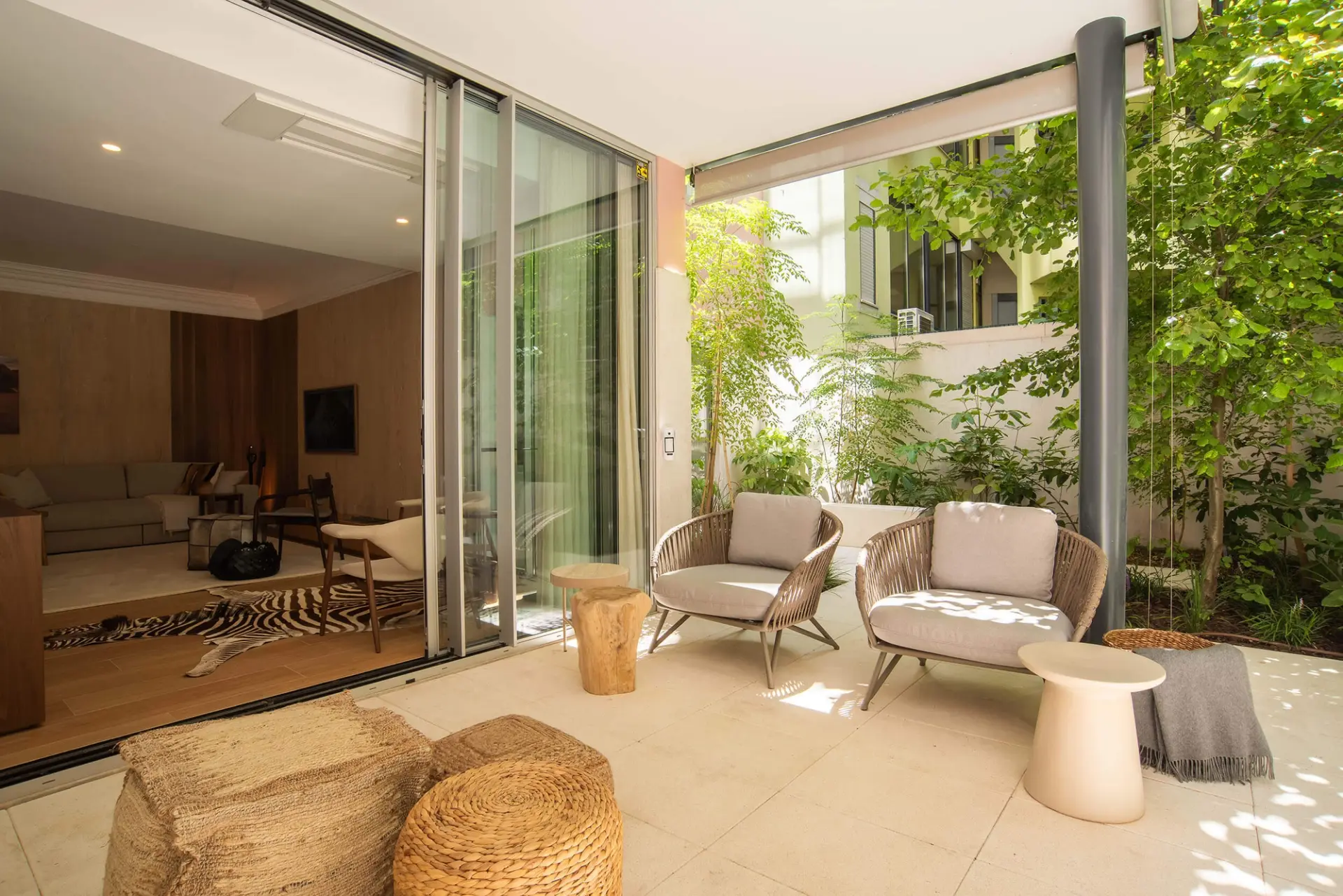Poltronas em corda entrançada com almofadas claras, pufes em fibra natural e pátio interior ajardinado envidraçado — exterior de luxo