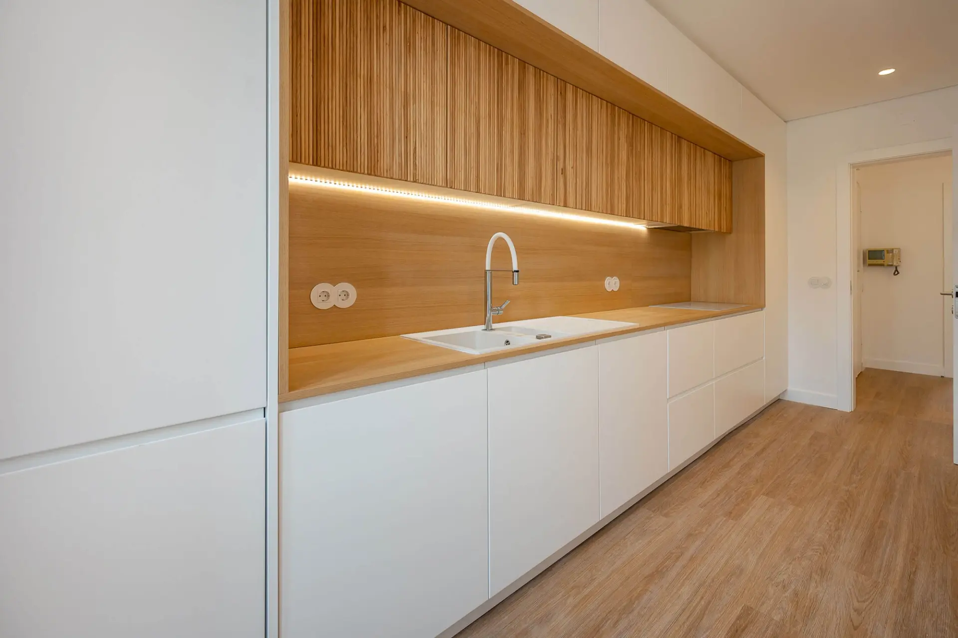 Fluted oak upper cabinet, oak backsplash and worktop over white base units with a concealed LED strip — luxury kitchen
