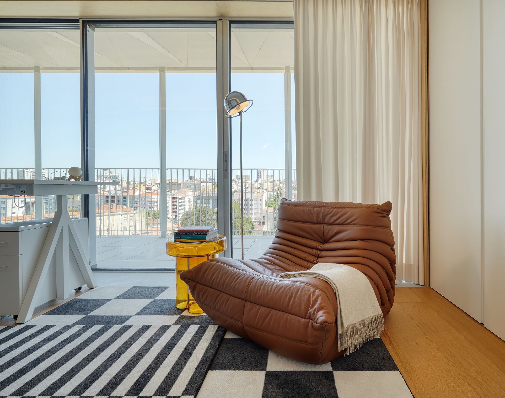 Zona de leitura com cadeirão Togo em couro cognac, mesa amarela e vista sobre Lisboa — design de interiores de luxo, Praça de Espanha, Atelier Renata Santos Machado