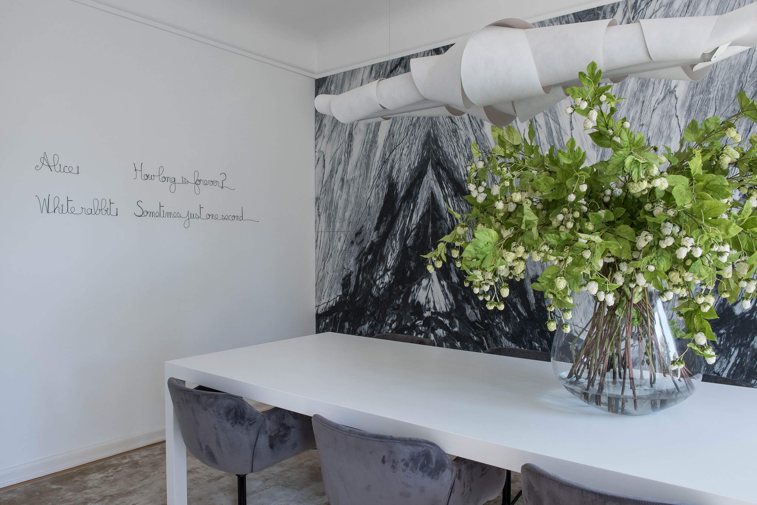 White Corian table and a spiral Foscarini Jamaica pendant against a black-and-white marble photographic mural — luxury dining room
