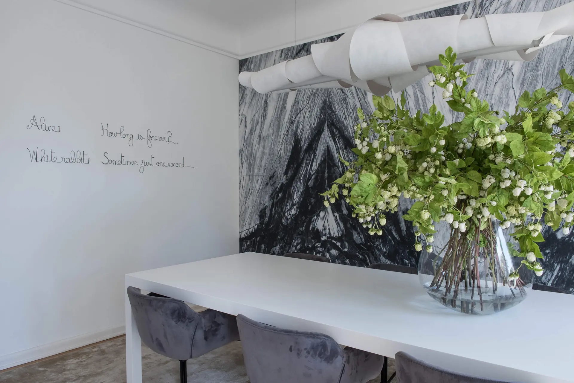 White Corian table and a spiral Foscarini Jamaica pendant against a black-and-white marble photographic mural — luxury dining room