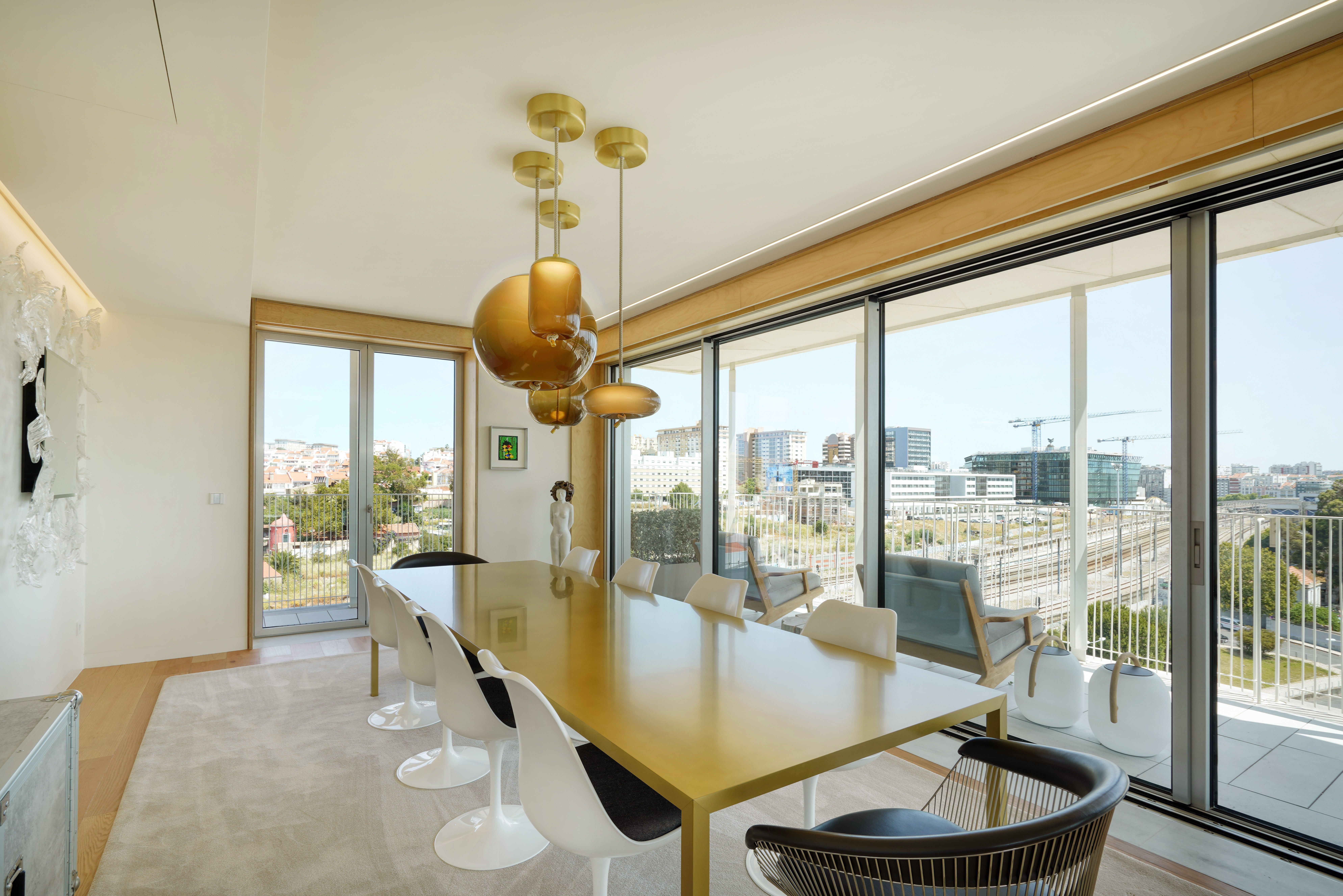 Sala de jantar de projeto de design de interiores em Lisboa, com mesa dourada, iluminação suspensa e grandes janelas.
