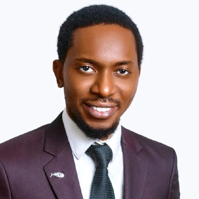 Israel Imasuen smiling, wearing a burgundy jacket and tie