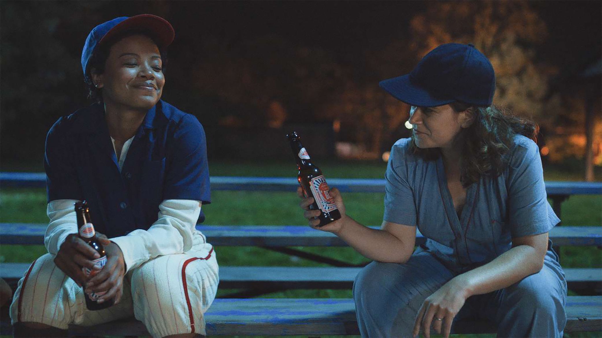 Carson and Max drink a beer together on a bleacher at night.