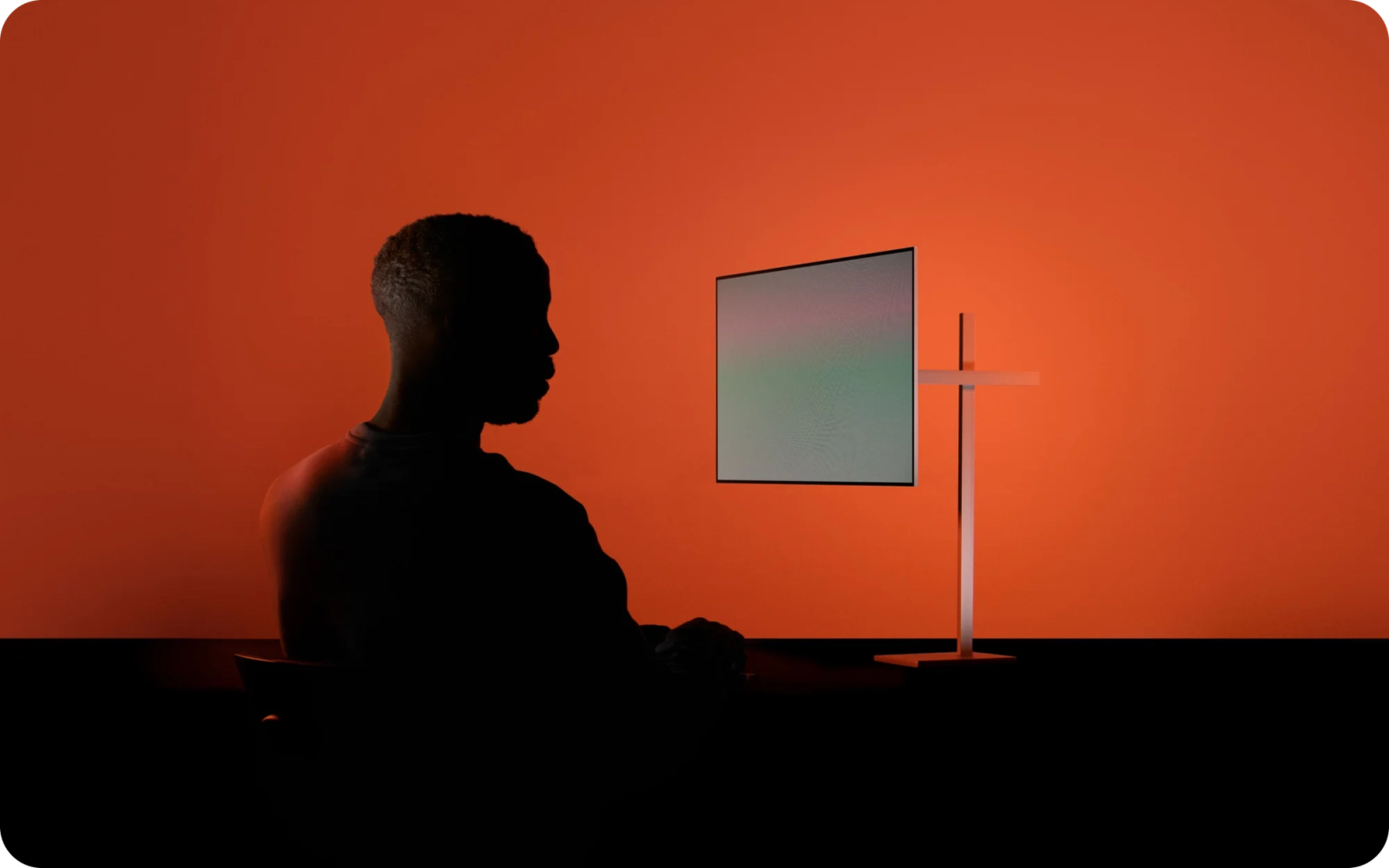 Silhouette of a person facing a computer monitor on an orange background