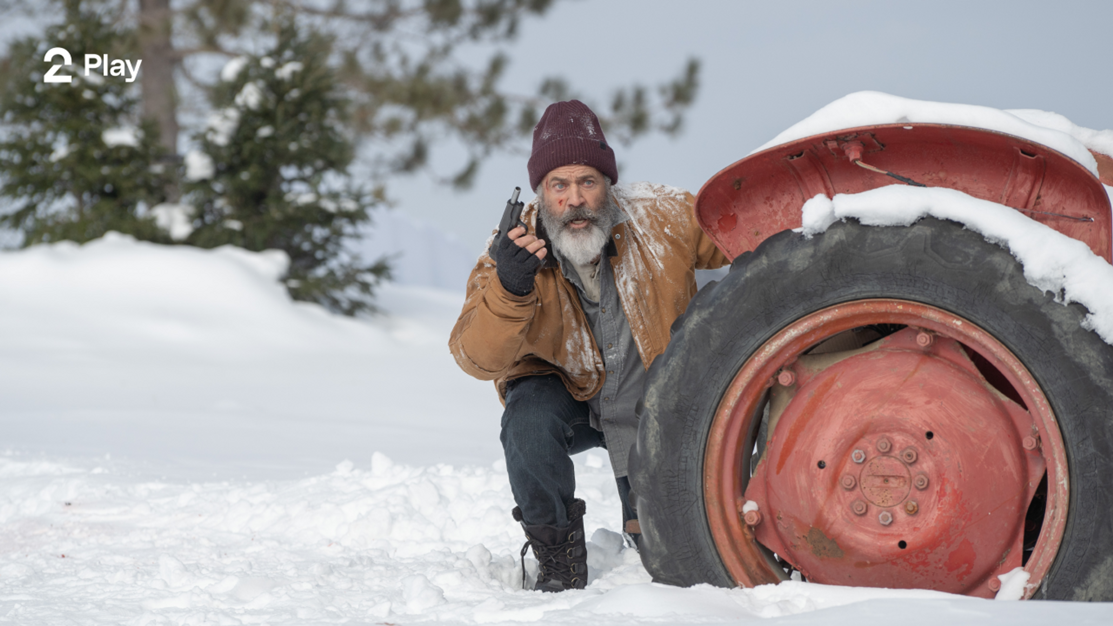 En mann gjemmer seg bak en traktor i et snødekt landskap mens han holder en pistol