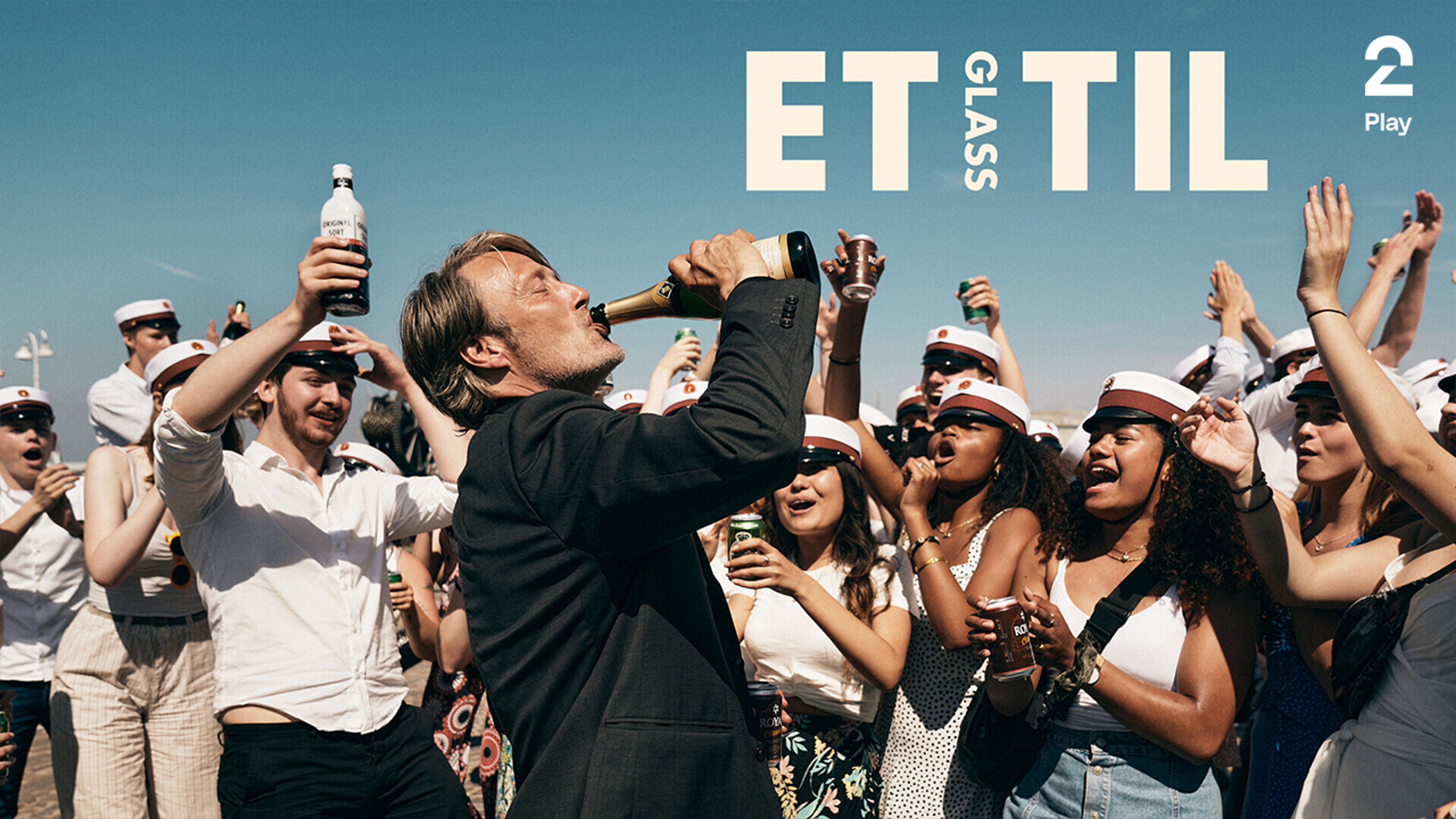 Mann drikker av en flaske champagne omringet av jublende studenter