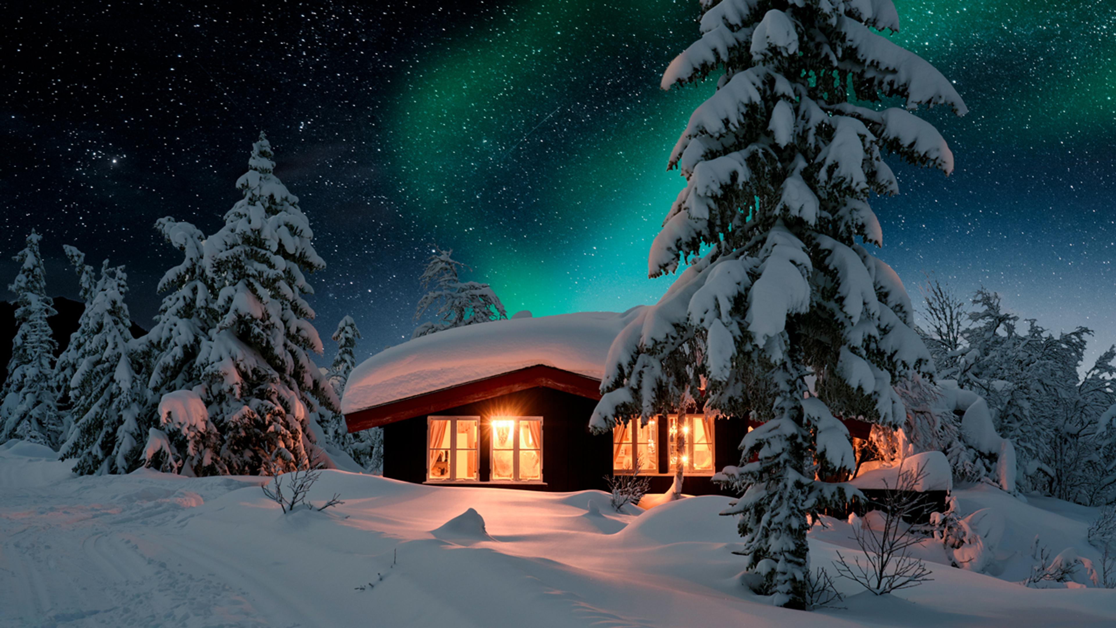 Hytte i vinterlandskap. Masse snø, nordlys og stjerner på himmelen og lys som kommer fra vinduene.
