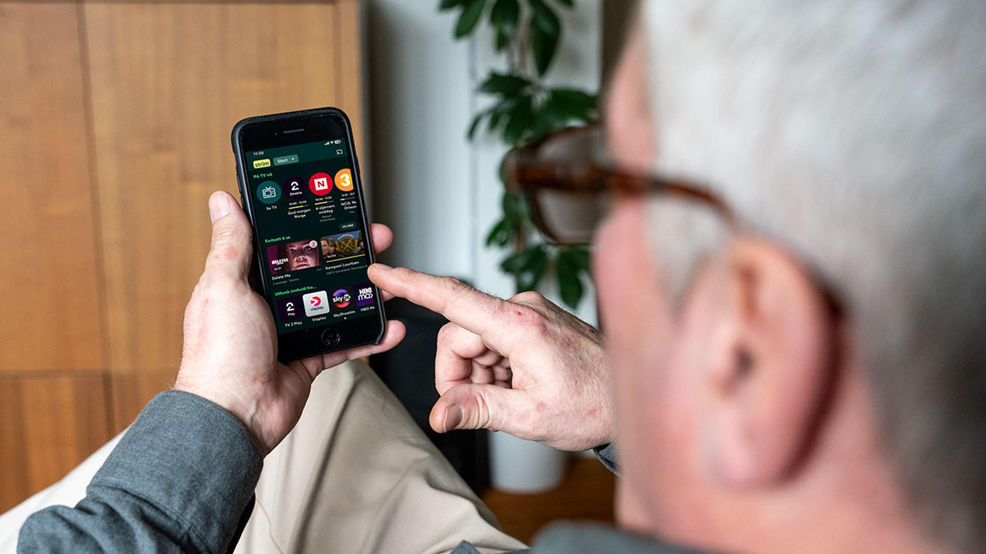 Mann bruker telefon for å se TV med Strim-appen.