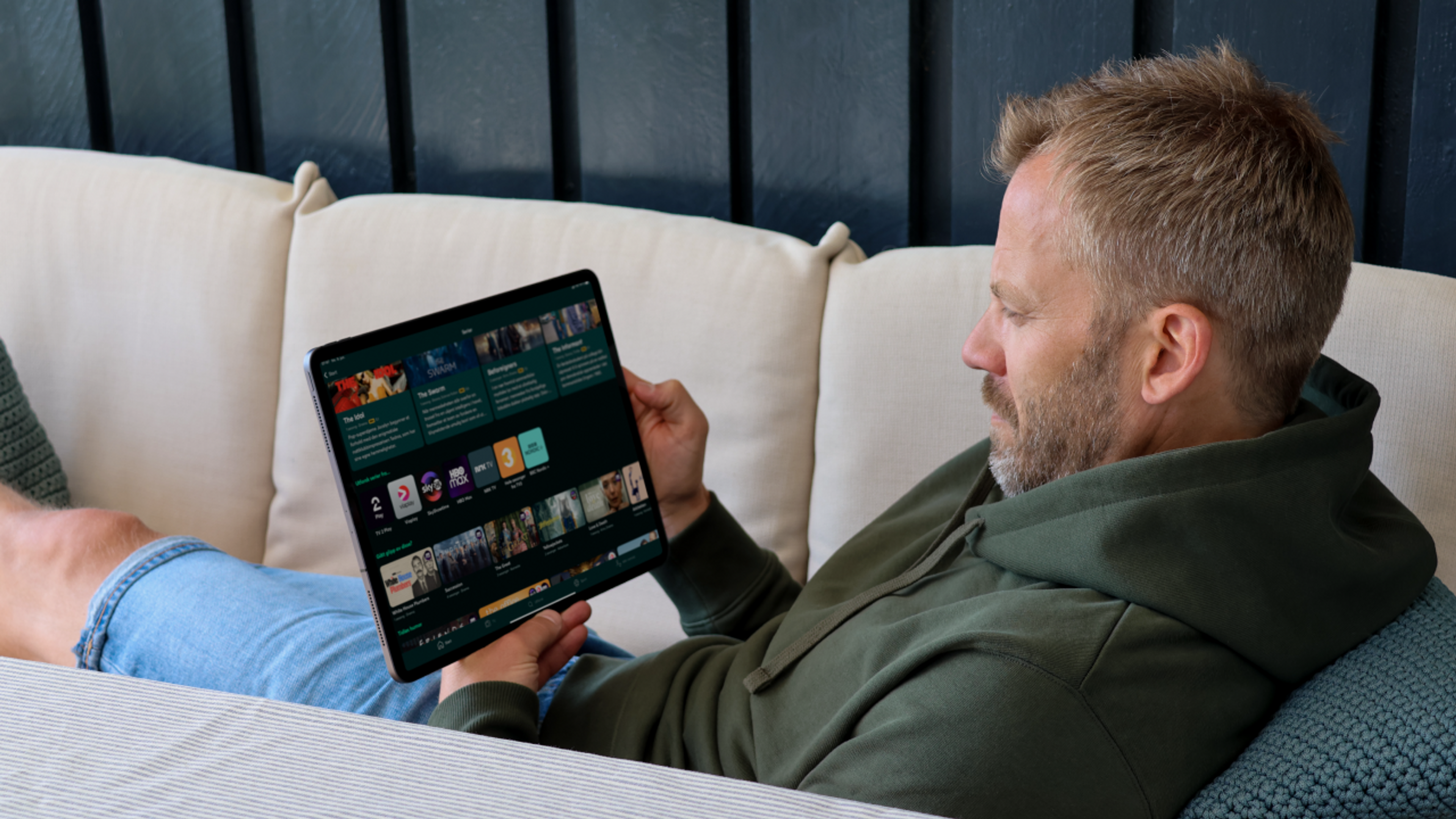 Mann blar seg igjennom innholdet i Strim-appen på nettbrett mens han ligger i en sofa.