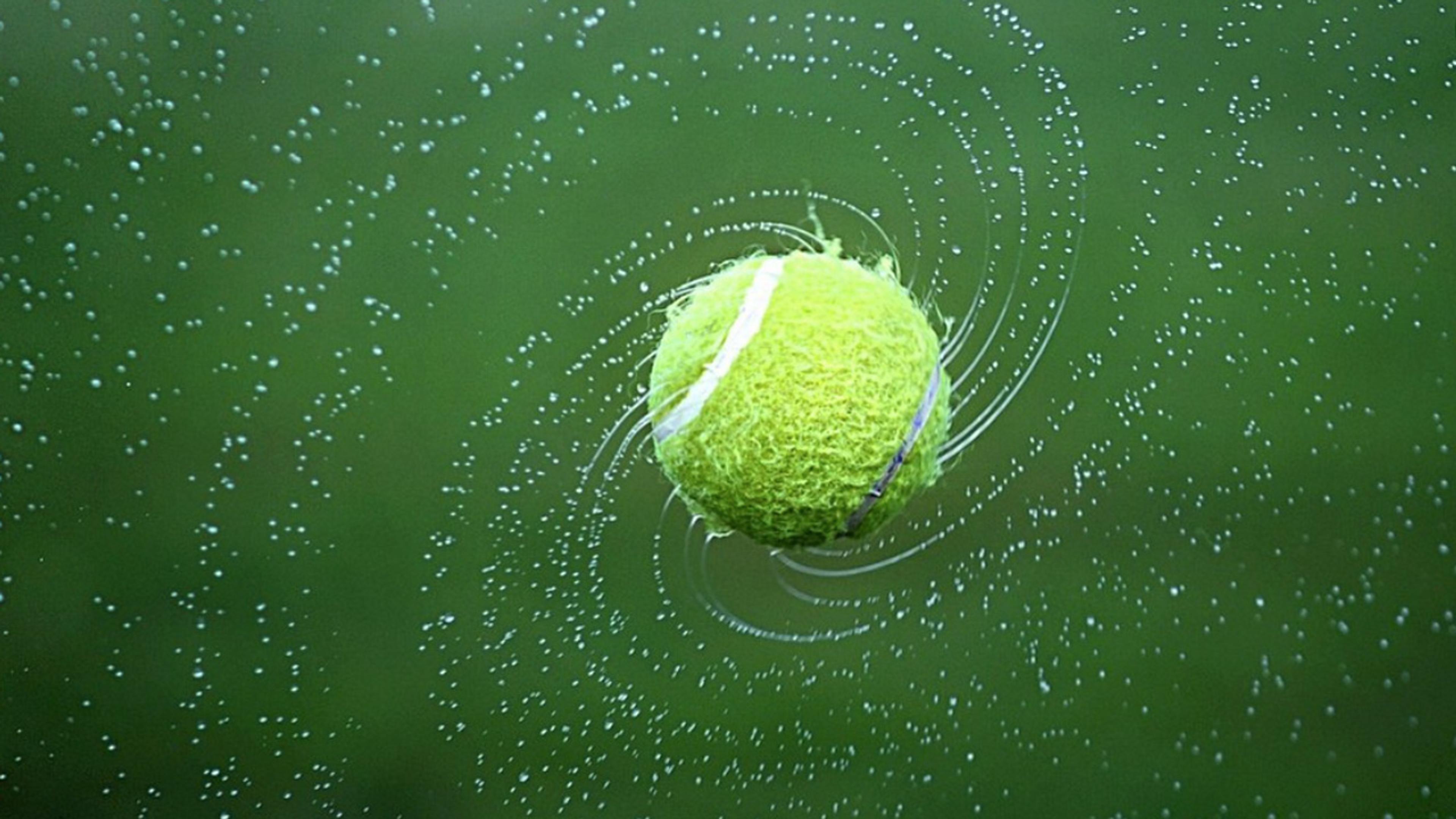 Tennisball som spinner rundt i luften mens vannet fosser av den.