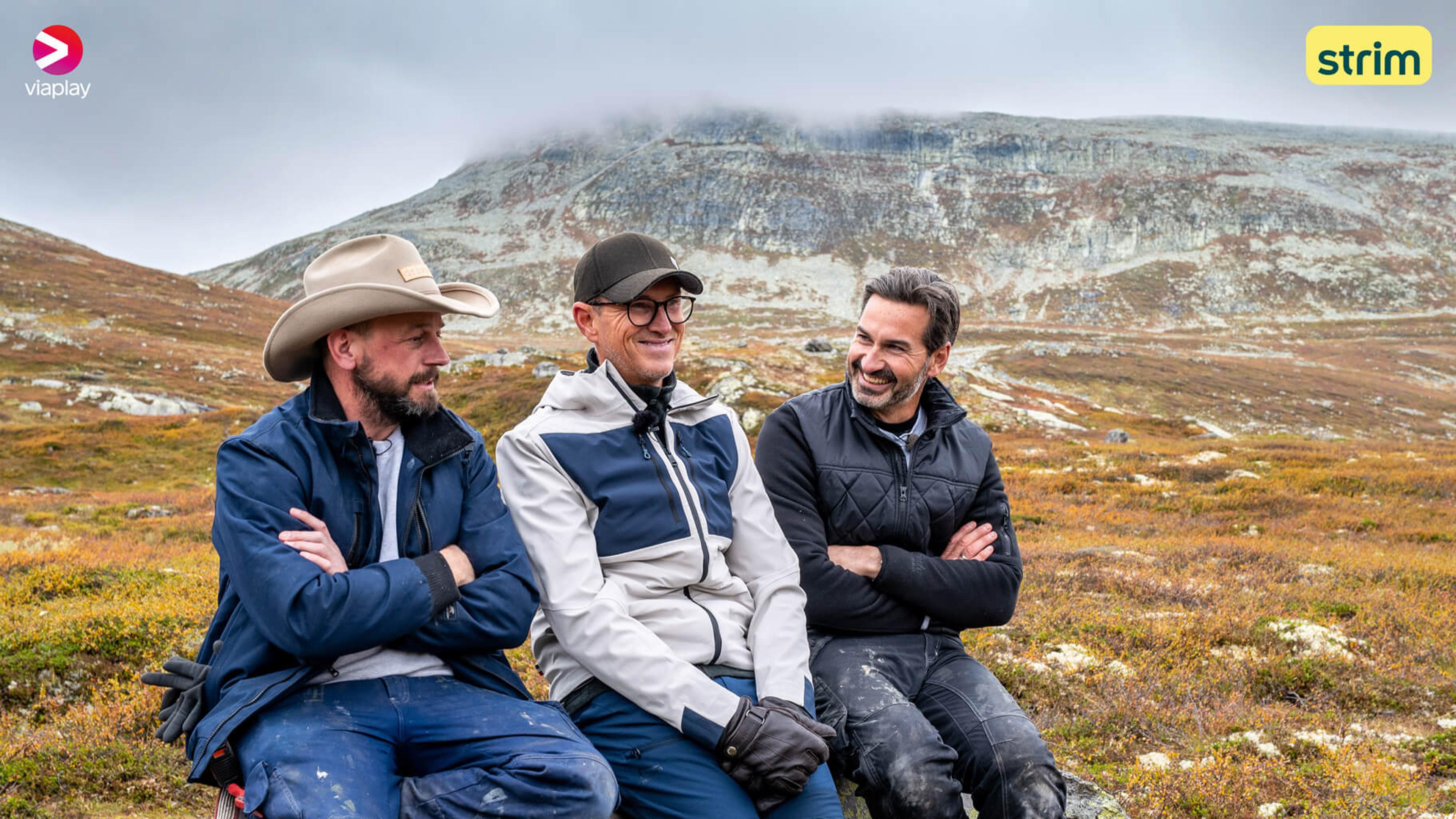 Programlederne fra Eventyrlig Oppussing sitter på en stein leende med fjellandskap i bakgrunnen. Se serien på Strim.