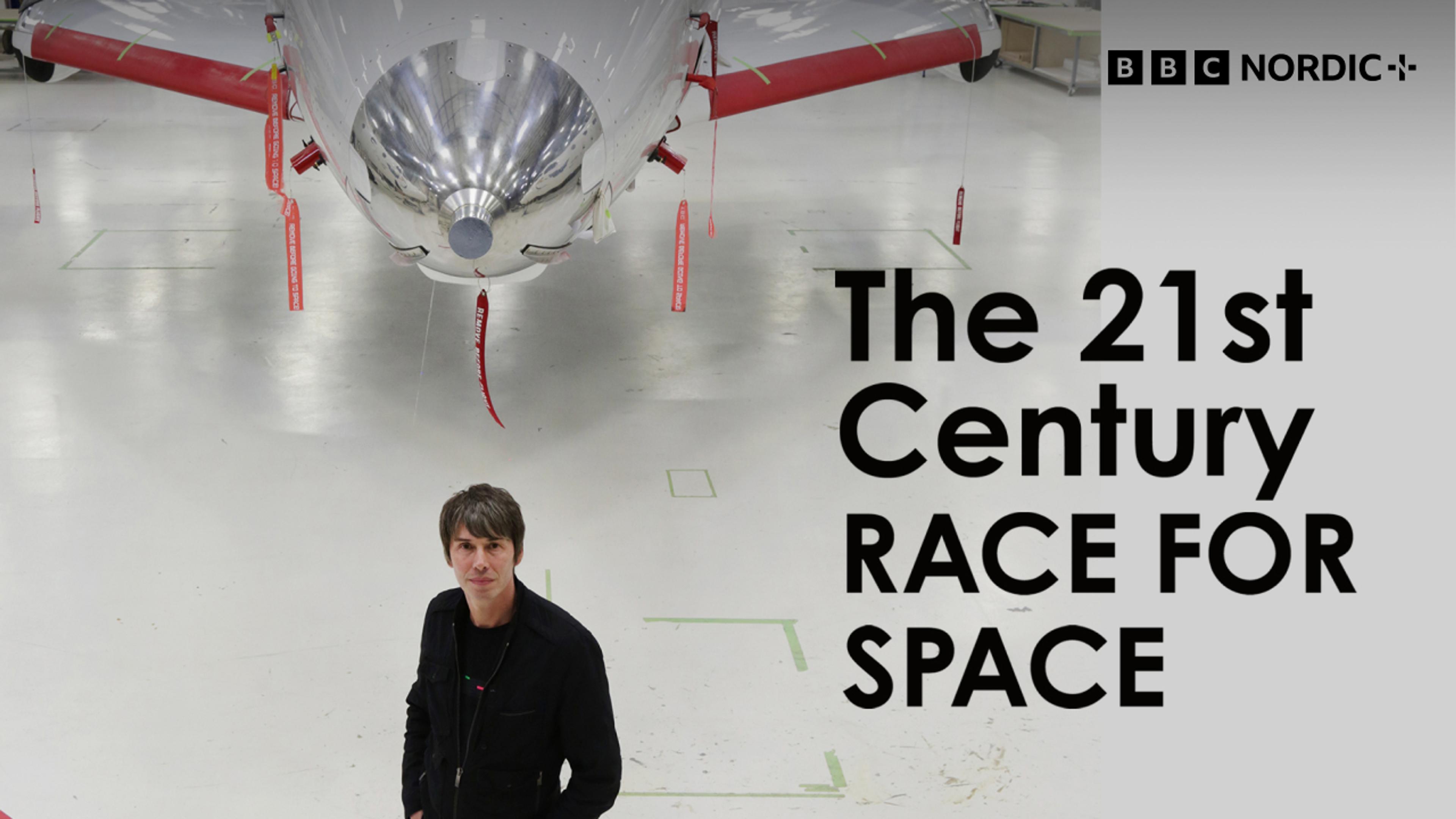 Brian Cox står foran et gammelt jagerfly i en hvit hangar.