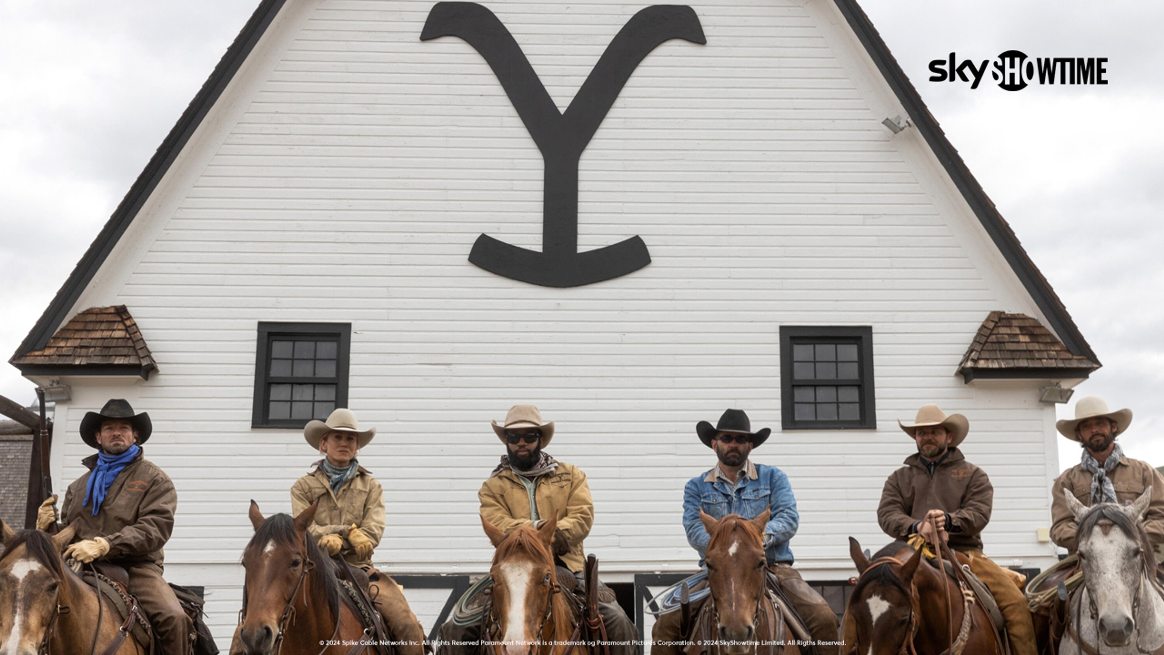 Cowboyene fra Yellowstone-serien står på rad og rekke på hestene sine foran Yellowstone gården.