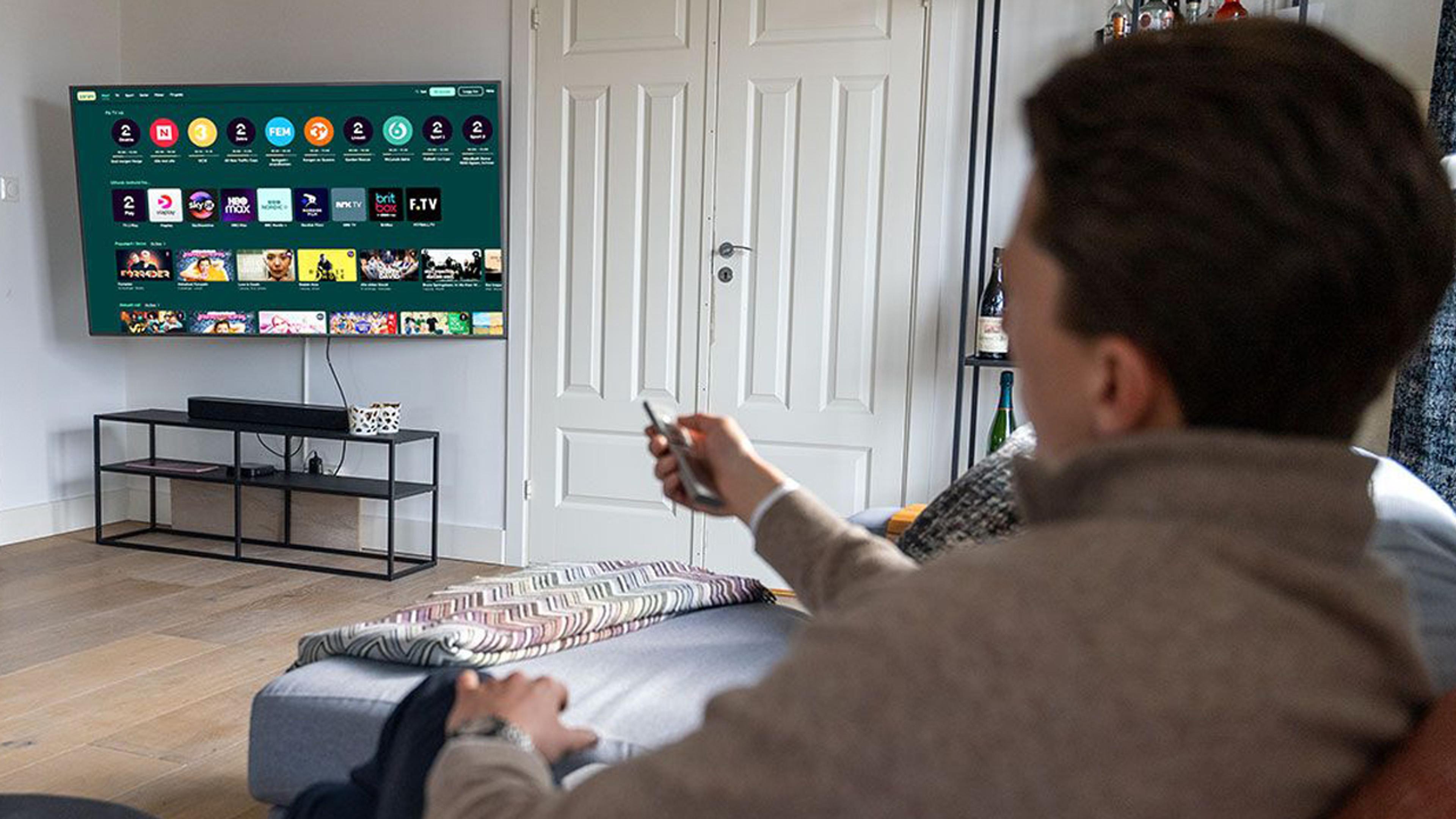 En mann sitter med en telefon i sofaen hvor Strims hjemskjerm vises
